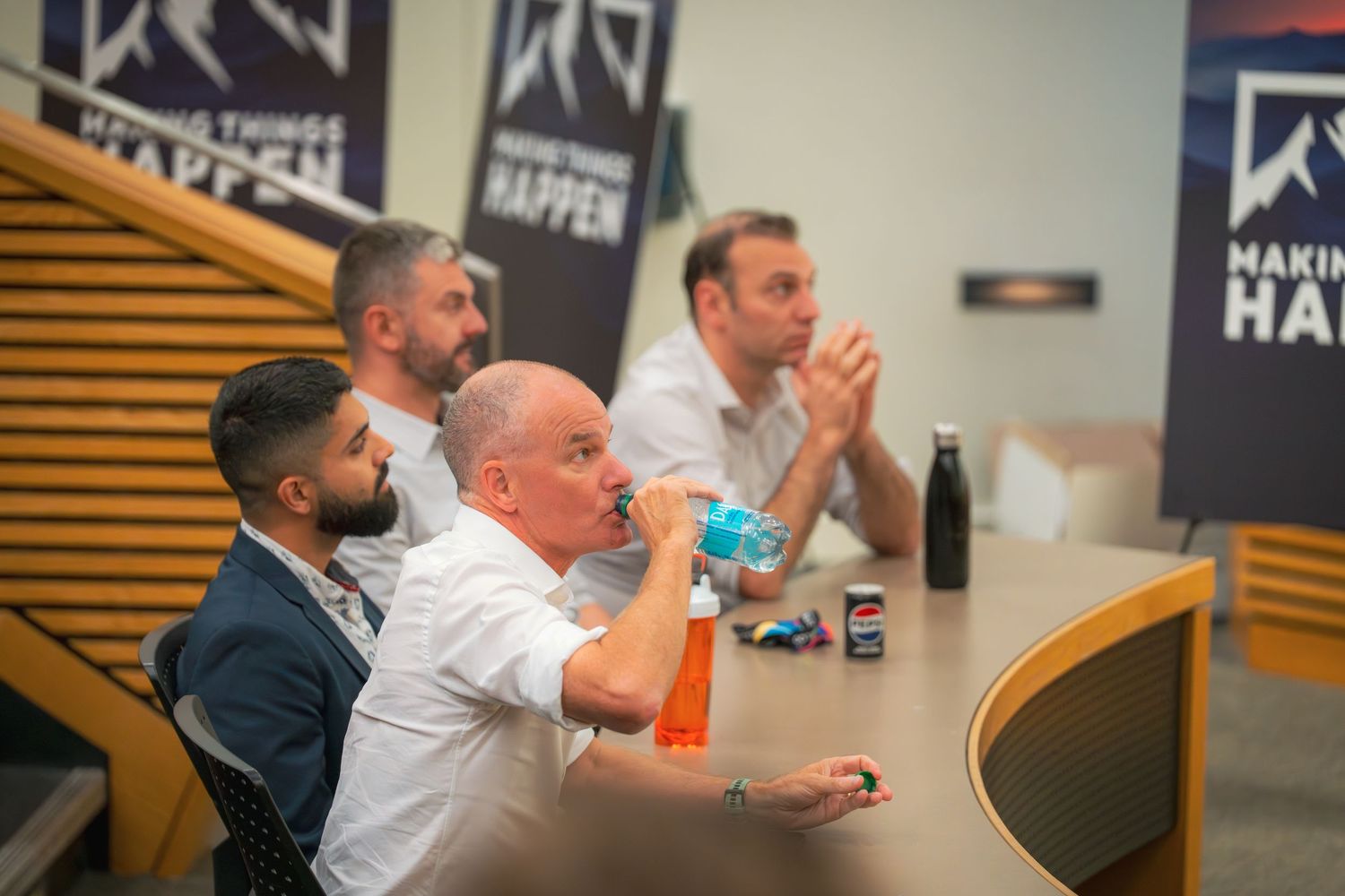 Attendees seated in a row during a business meeting with wooden paneled walls.