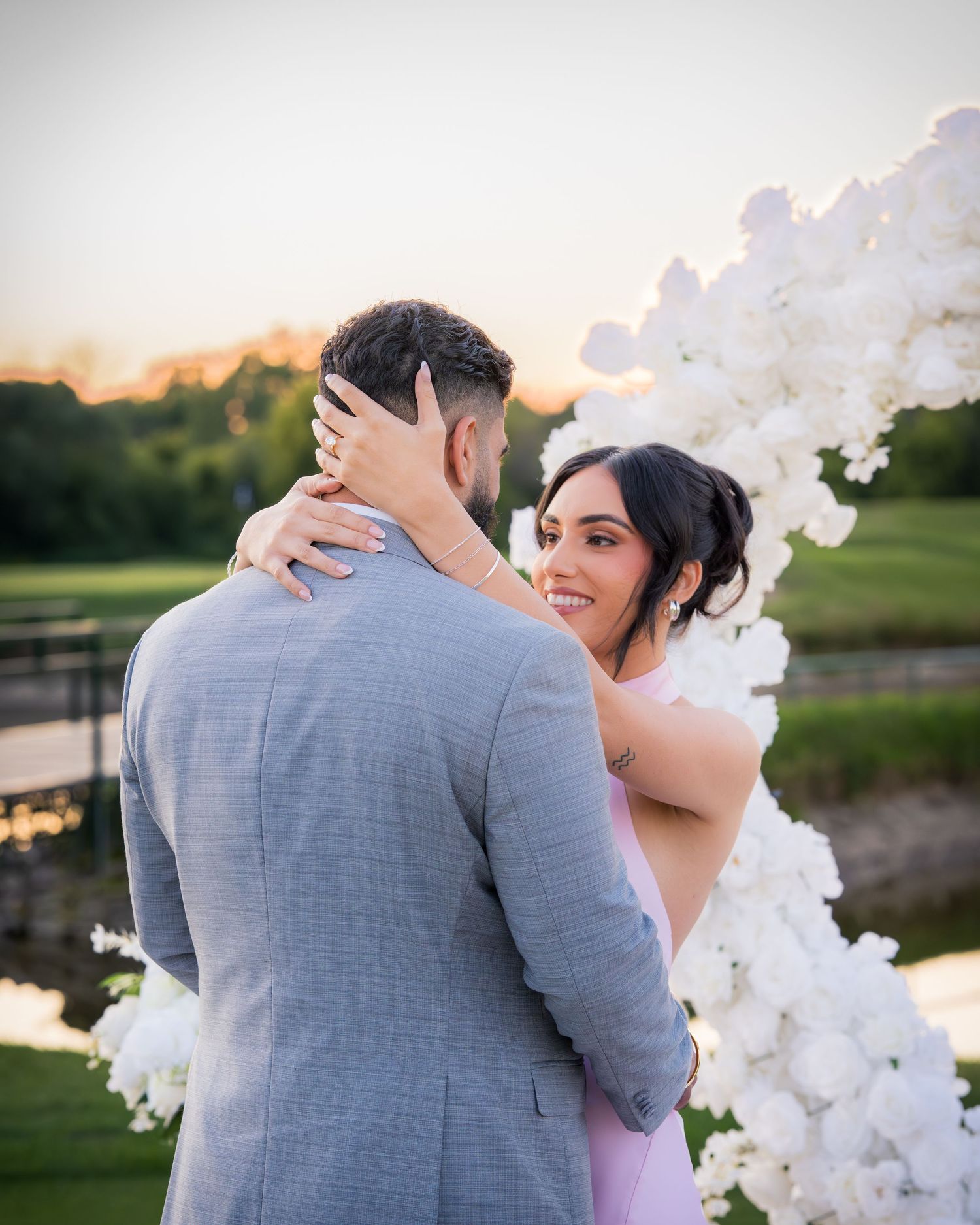 Intimate wedding moment captured under a decorative white arch during golden hour.