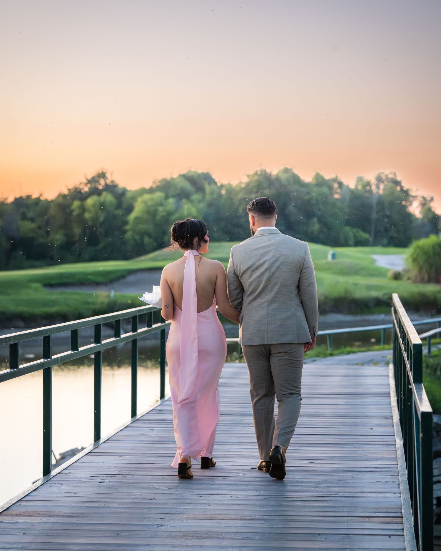 Two people walking hand in hand on a wooden boardwalk during sunset.