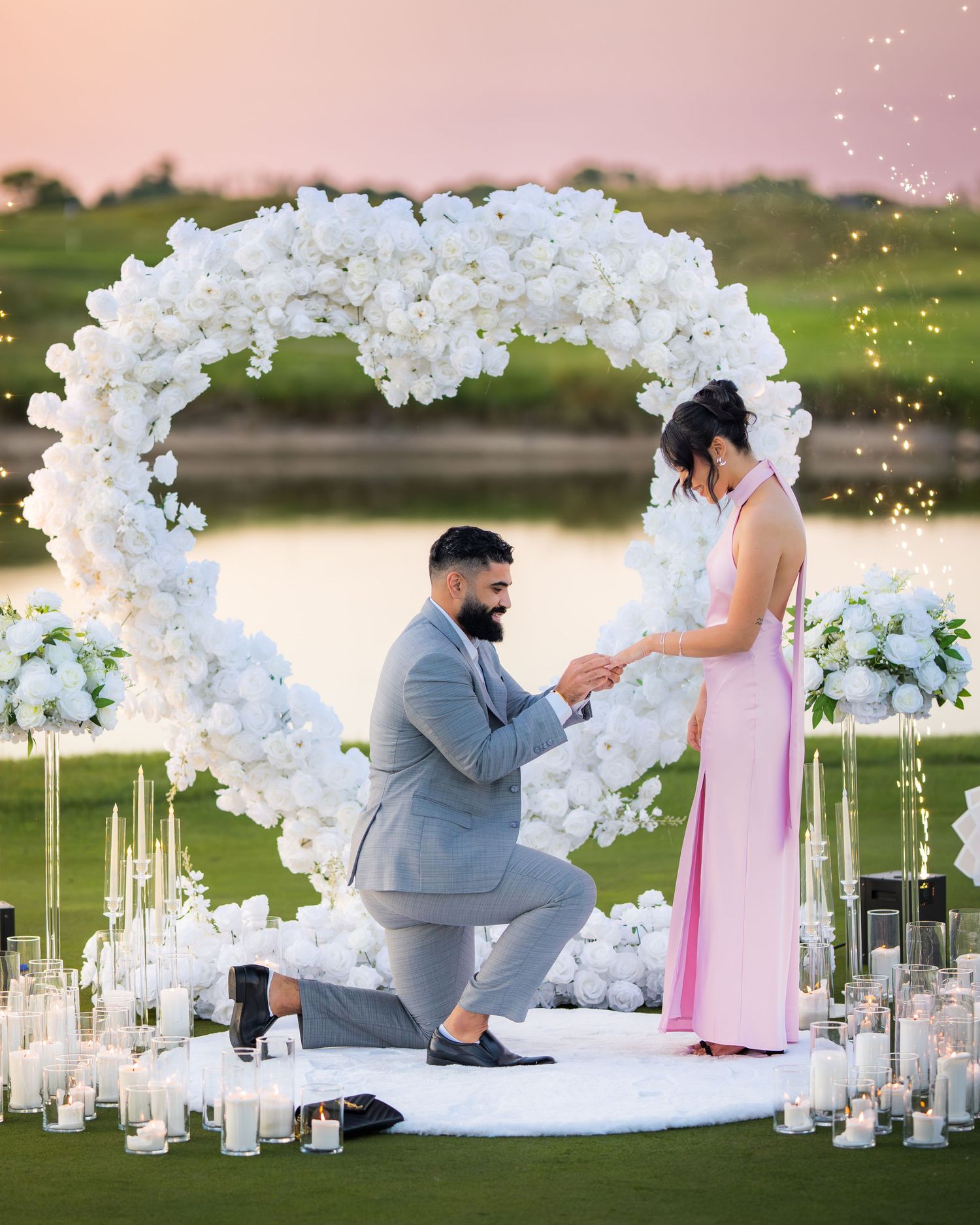 Magical proposal setting with white orchid arch and flickering candles by the water.