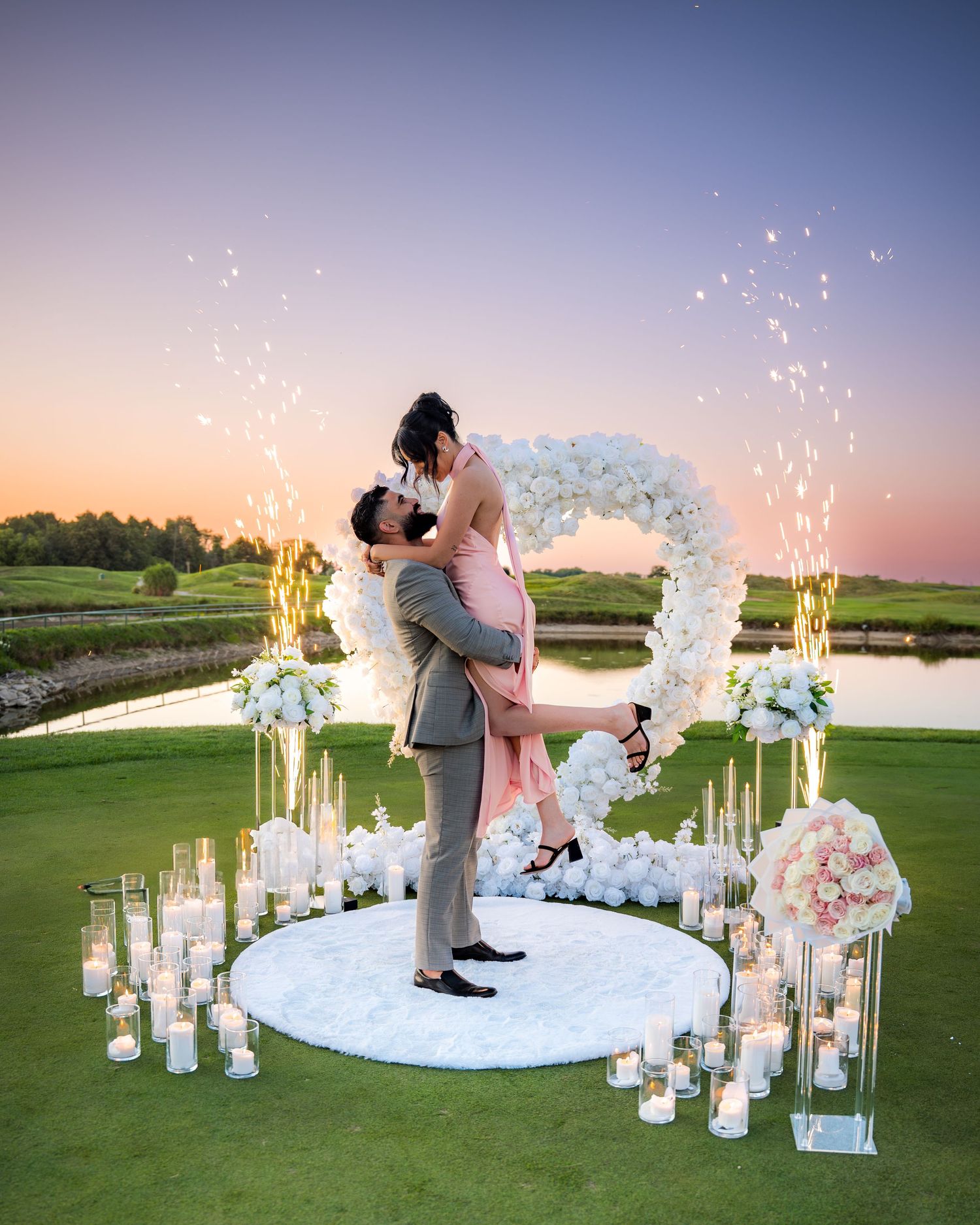 Sunset proposal scene with white floral decorations and sparkling fountains.
