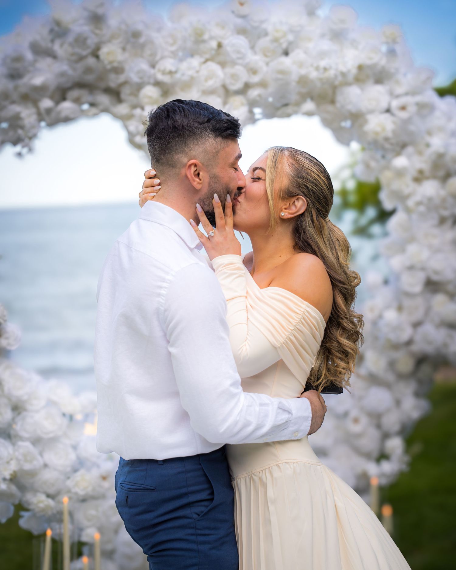 Celebration kiss under decorative white balloon arch by the ocean.