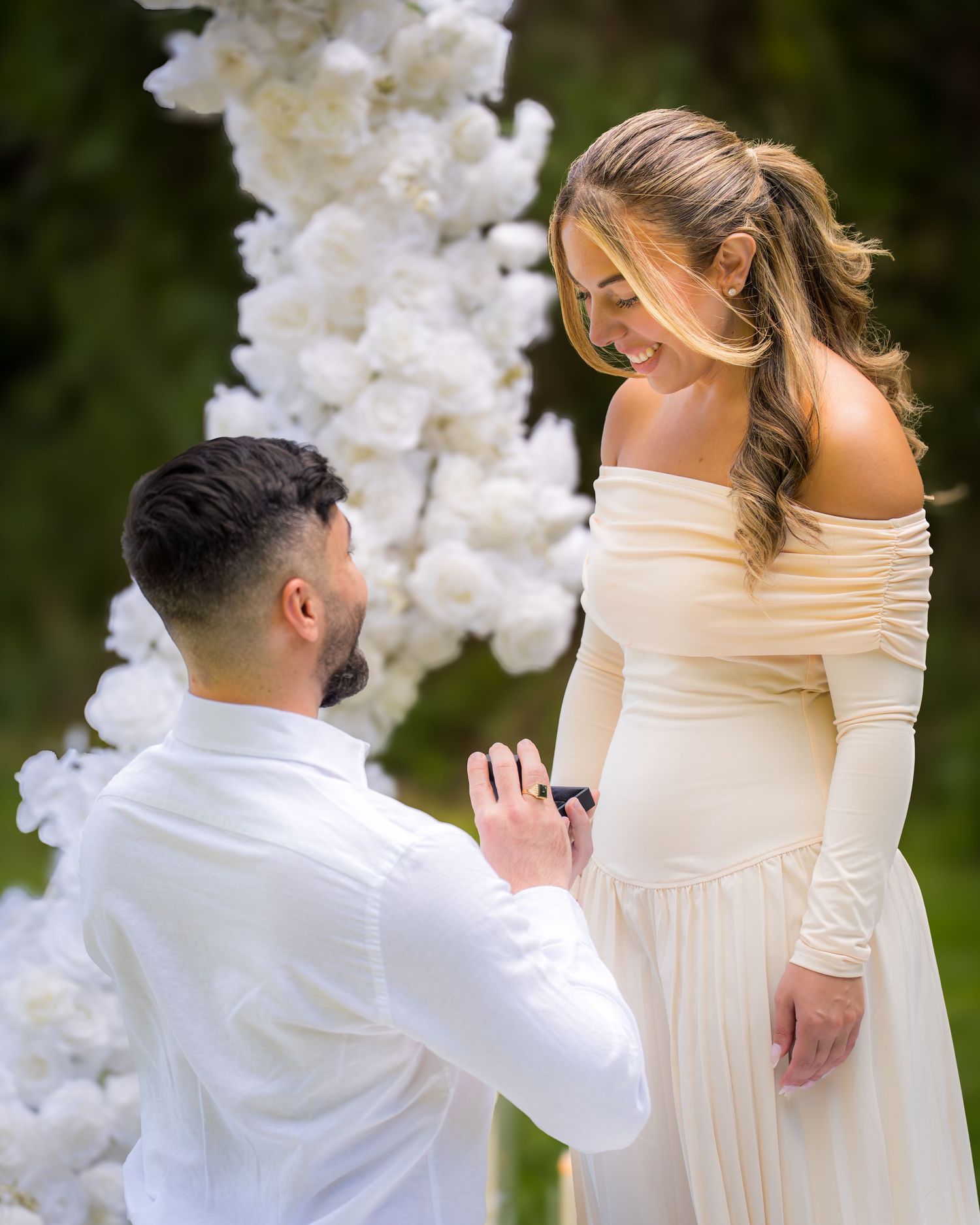 An emotional proposal moment captured in a garden setting with white floral decor.