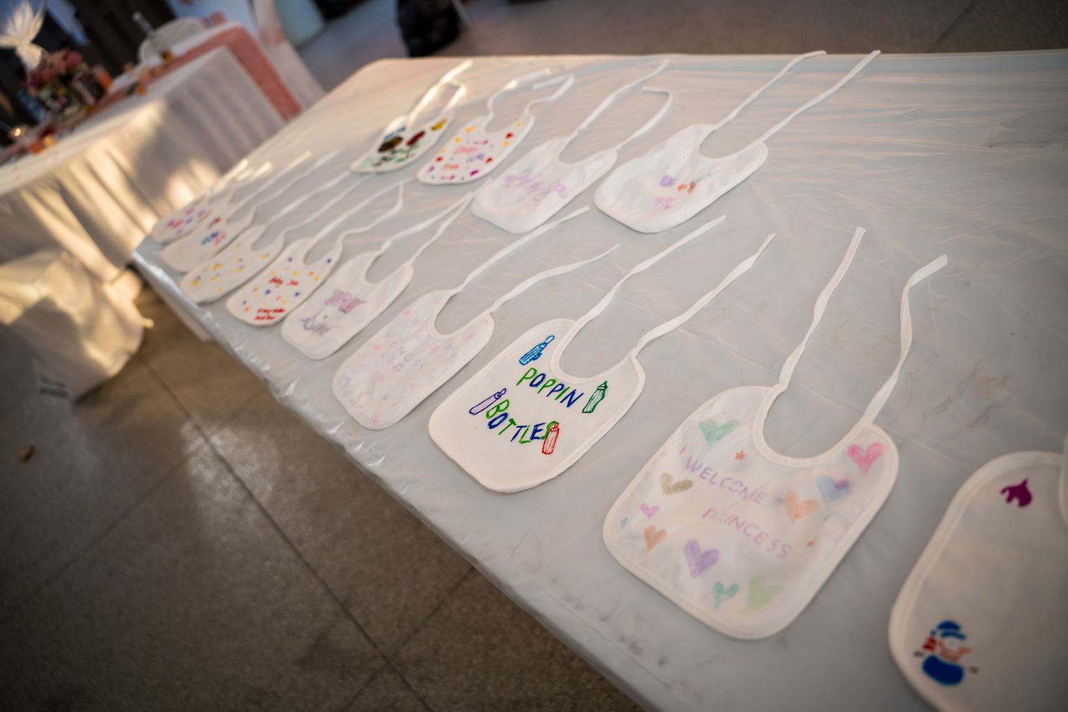 White baby bibs arranged in a line on the floor with colorful decorative designs.