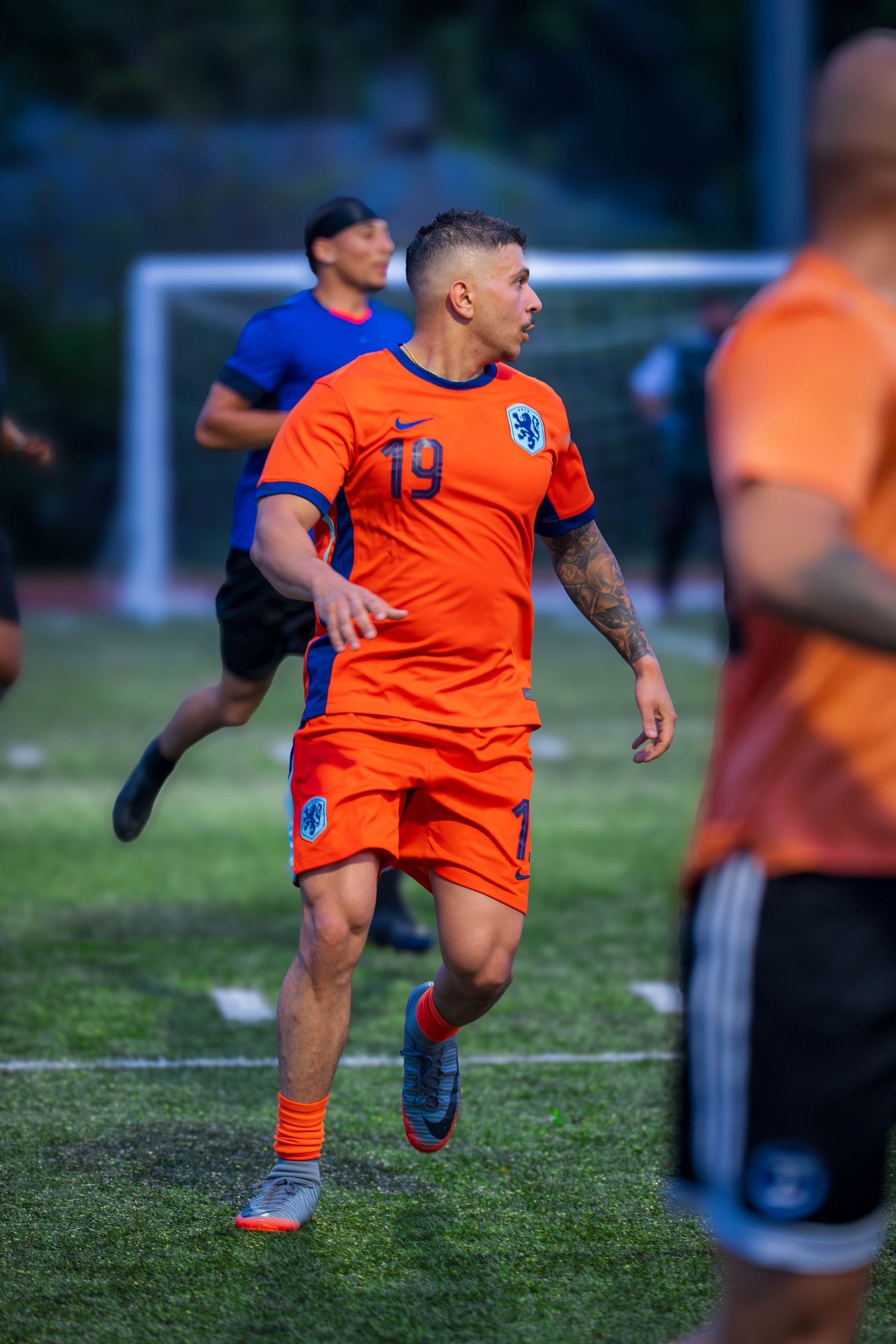 Soccer player in bright orange jersey number 19 runs on field during evening match.