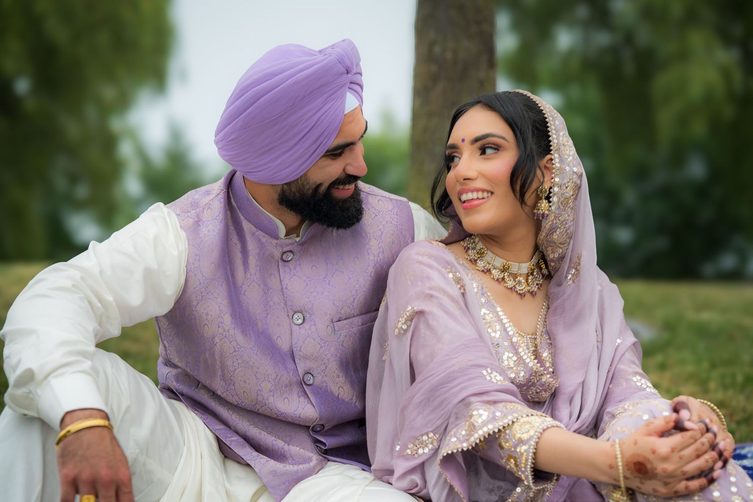 Couple in matching purple and white attire pose together outdoors against a natural backdrop.