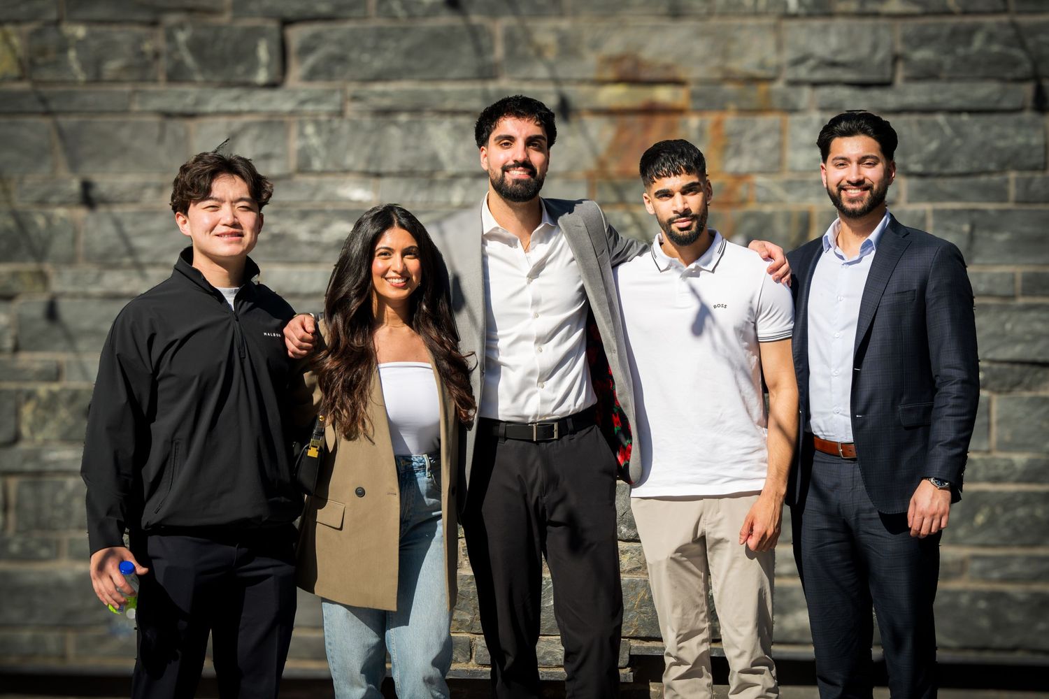 Friends standing together and smiling against a textured stone wall.