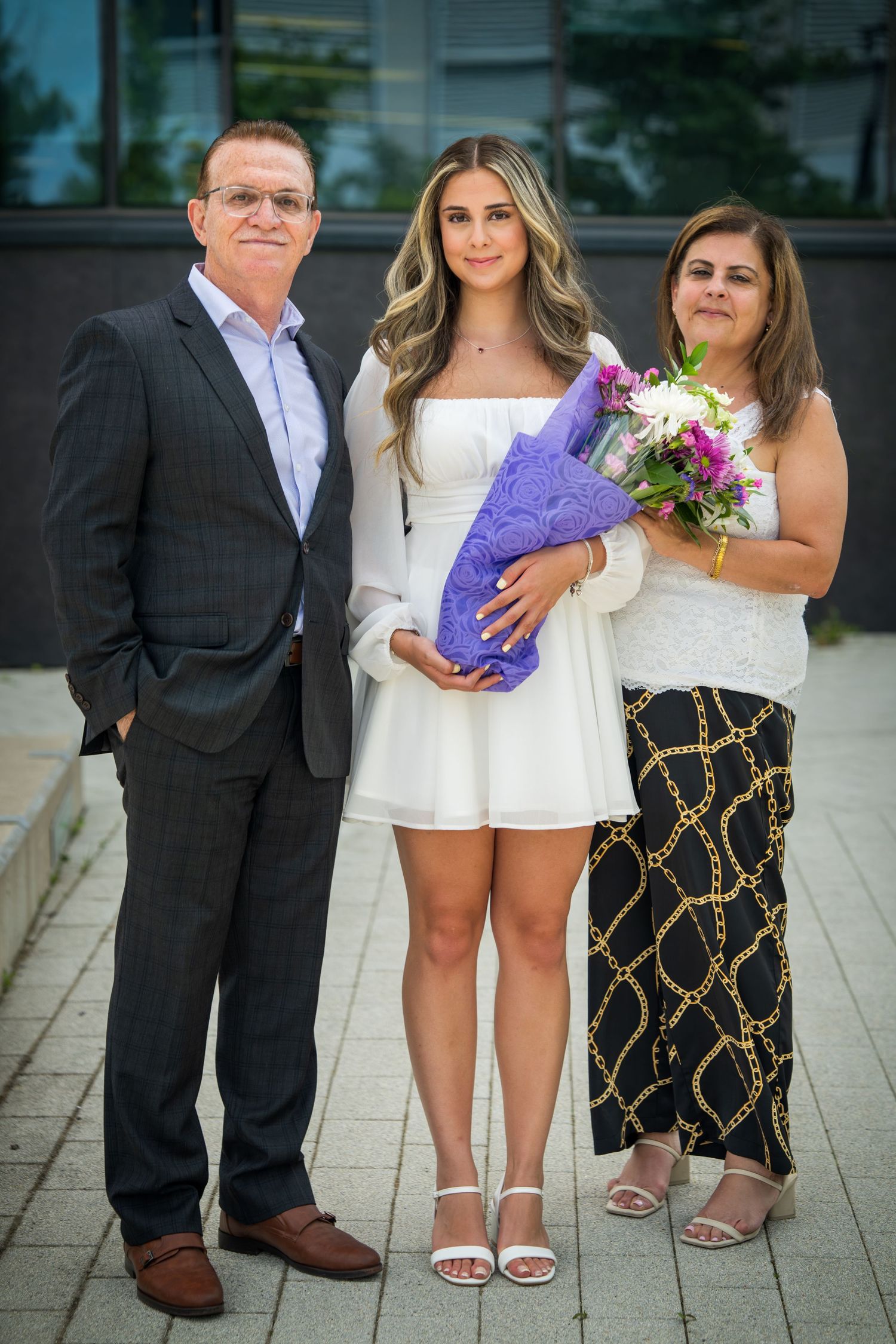 Group photo with people holding a purple gift box and flowers outdoors.