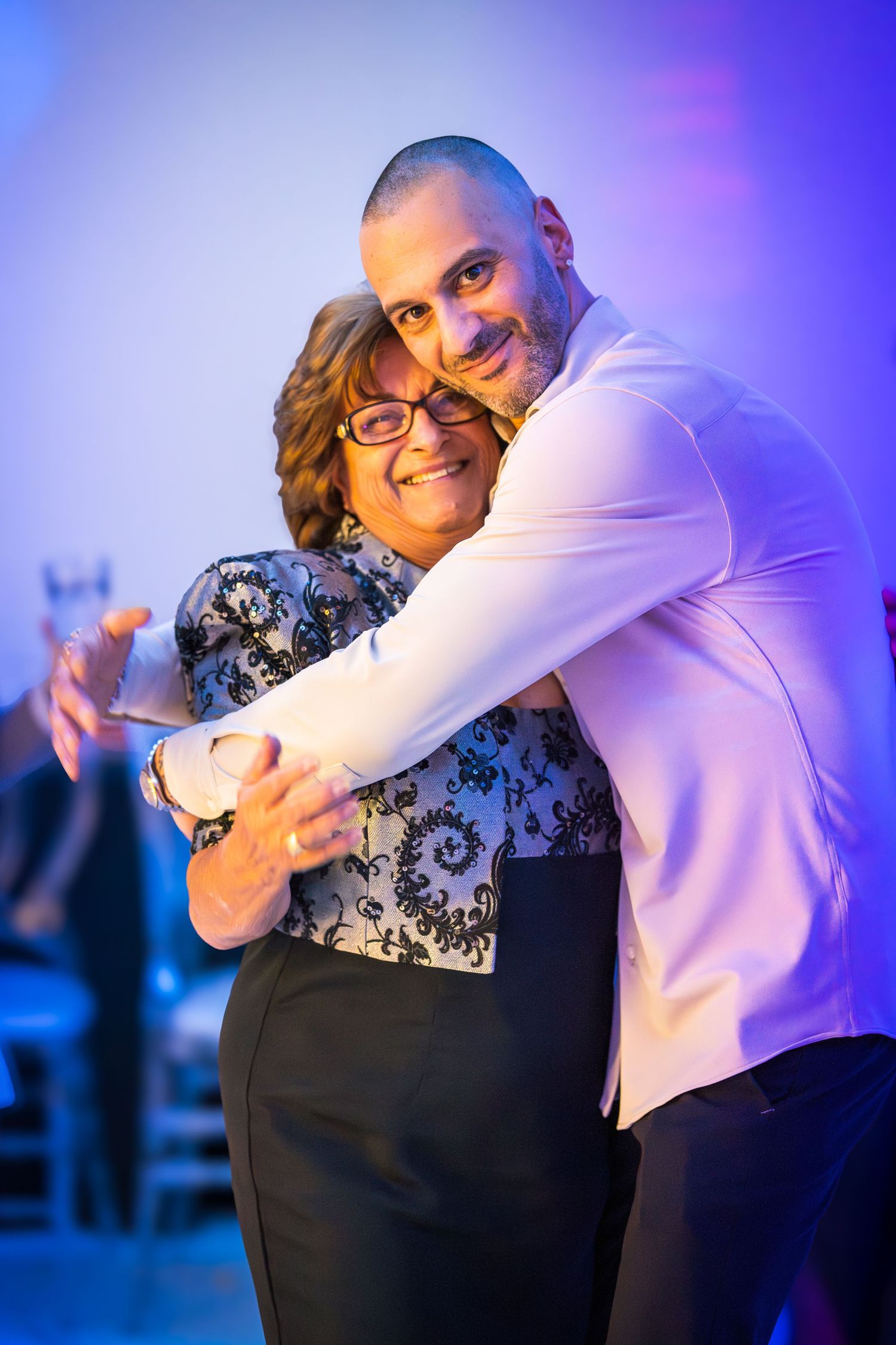 Two people sharing a warm embrace during a celebration with blue ambient lighting.