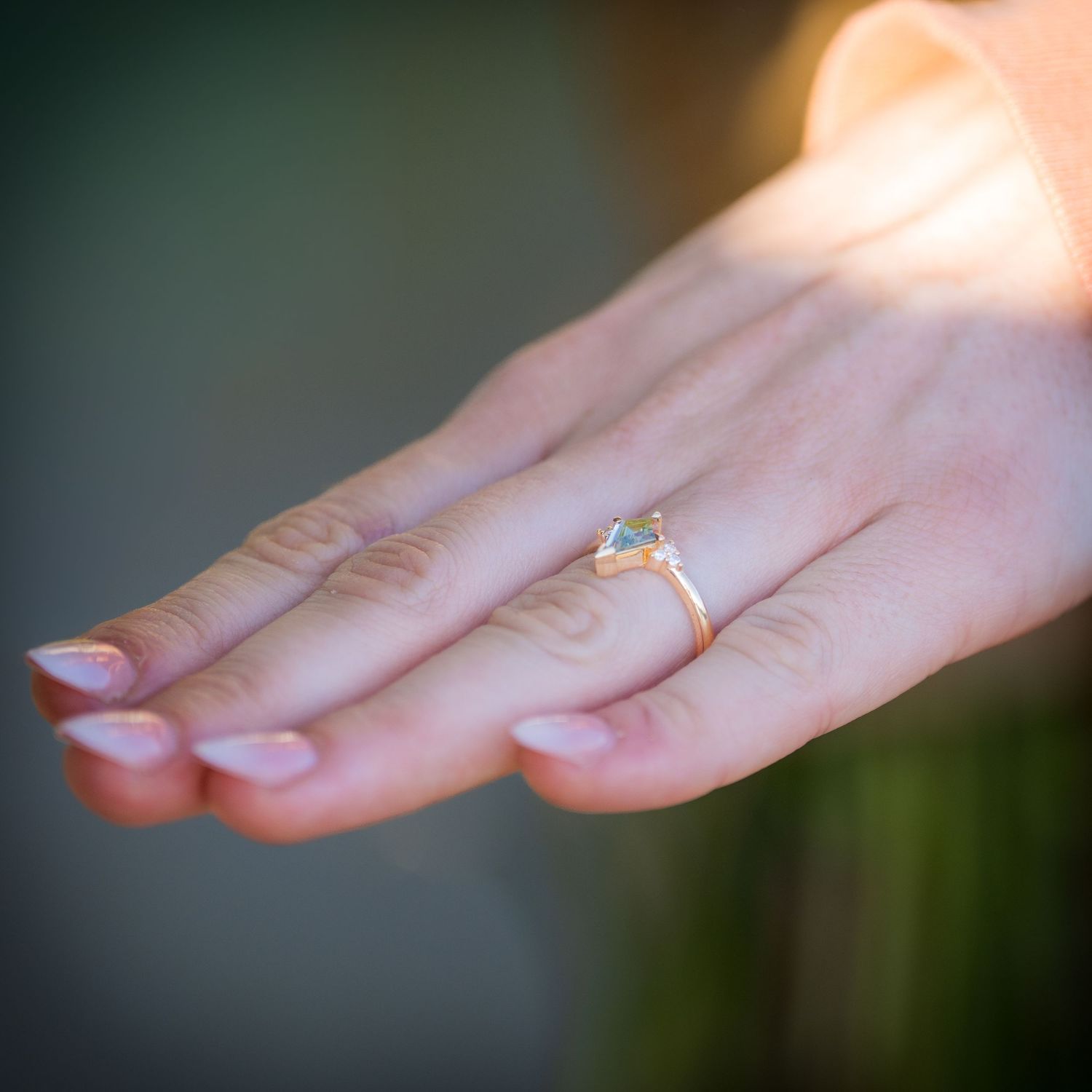 Close-up of a womans hand wearing a delicate gold ring with a blue gemstone in soft light.