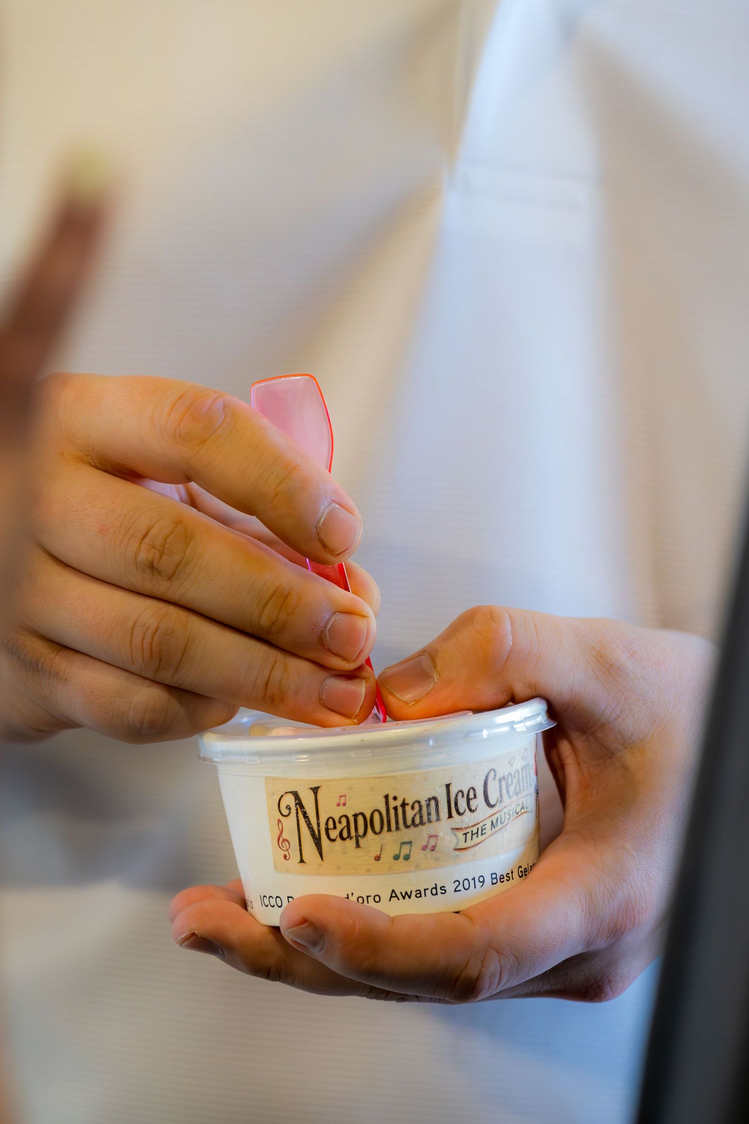 Close-up of hands holding a Neapolitan Ice Cream award cup with a pink spoon at a 2019 Gelato awards event.