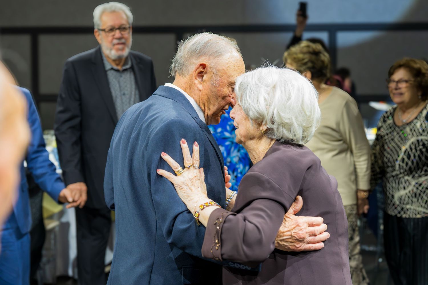 Elderly couple sharing a warm embrace while dancing together at a festive anniversary party celebration.