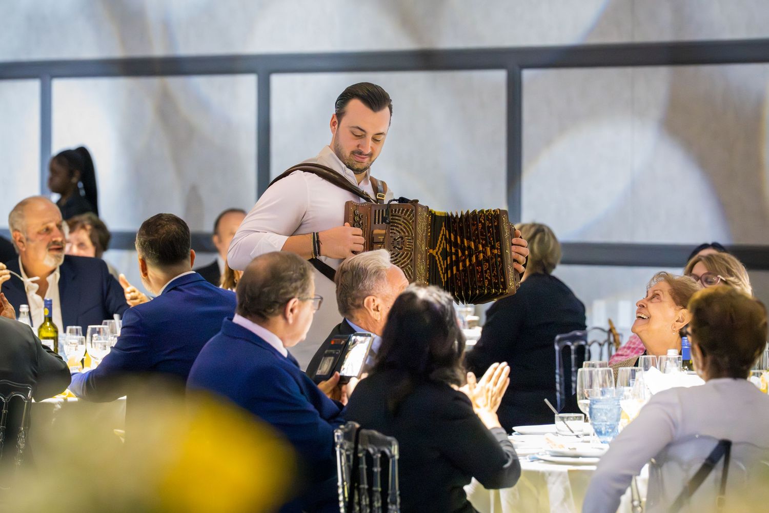 Accordion musician entertaining guests at an elegant wedding reception dinner with round tables.