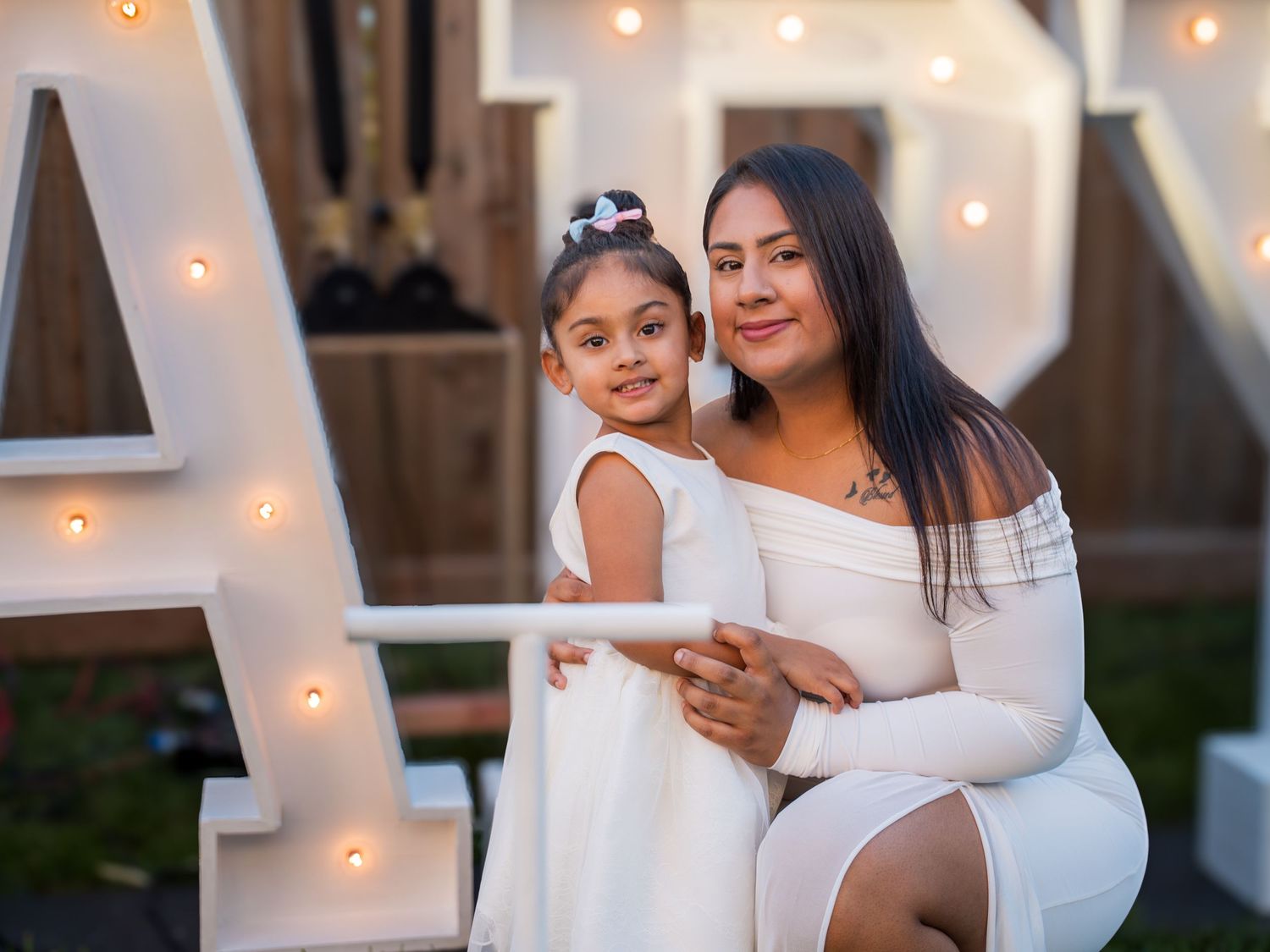 A woman and young girl in matching white dresses pose together at an elegant outdoor celebration.