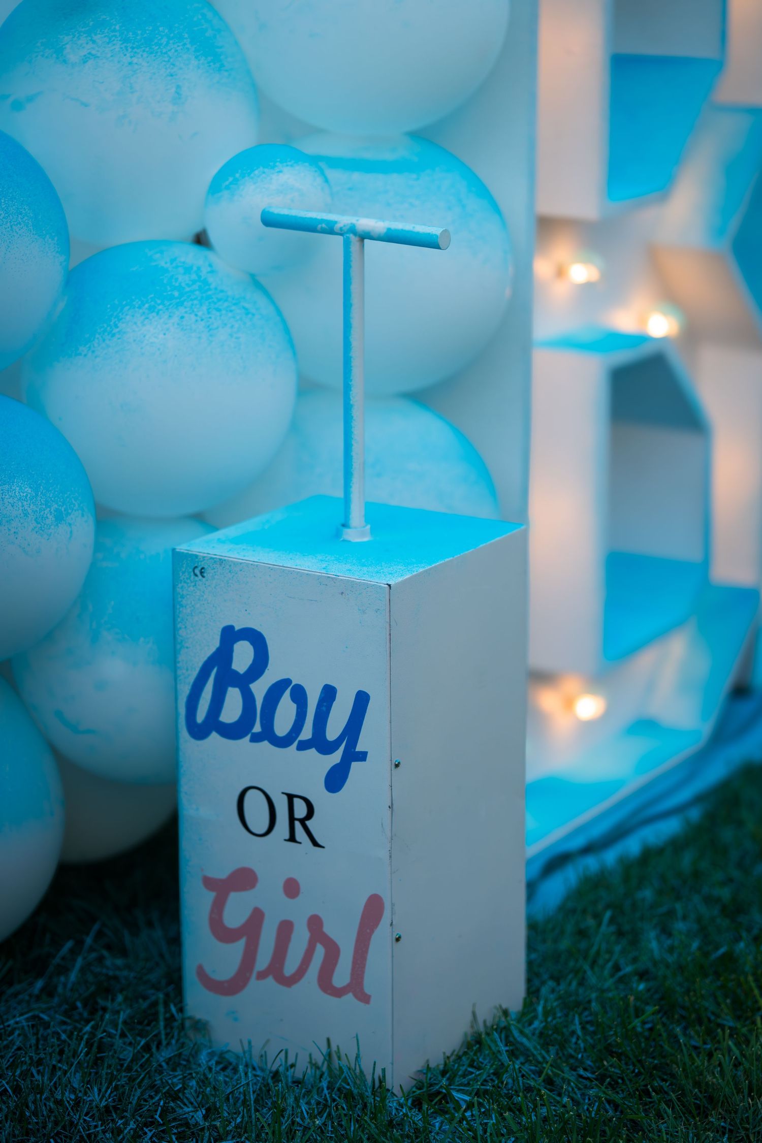 White Boy or Girl box with handle surrounded by blue-tinted balloons and marquee lights at night.