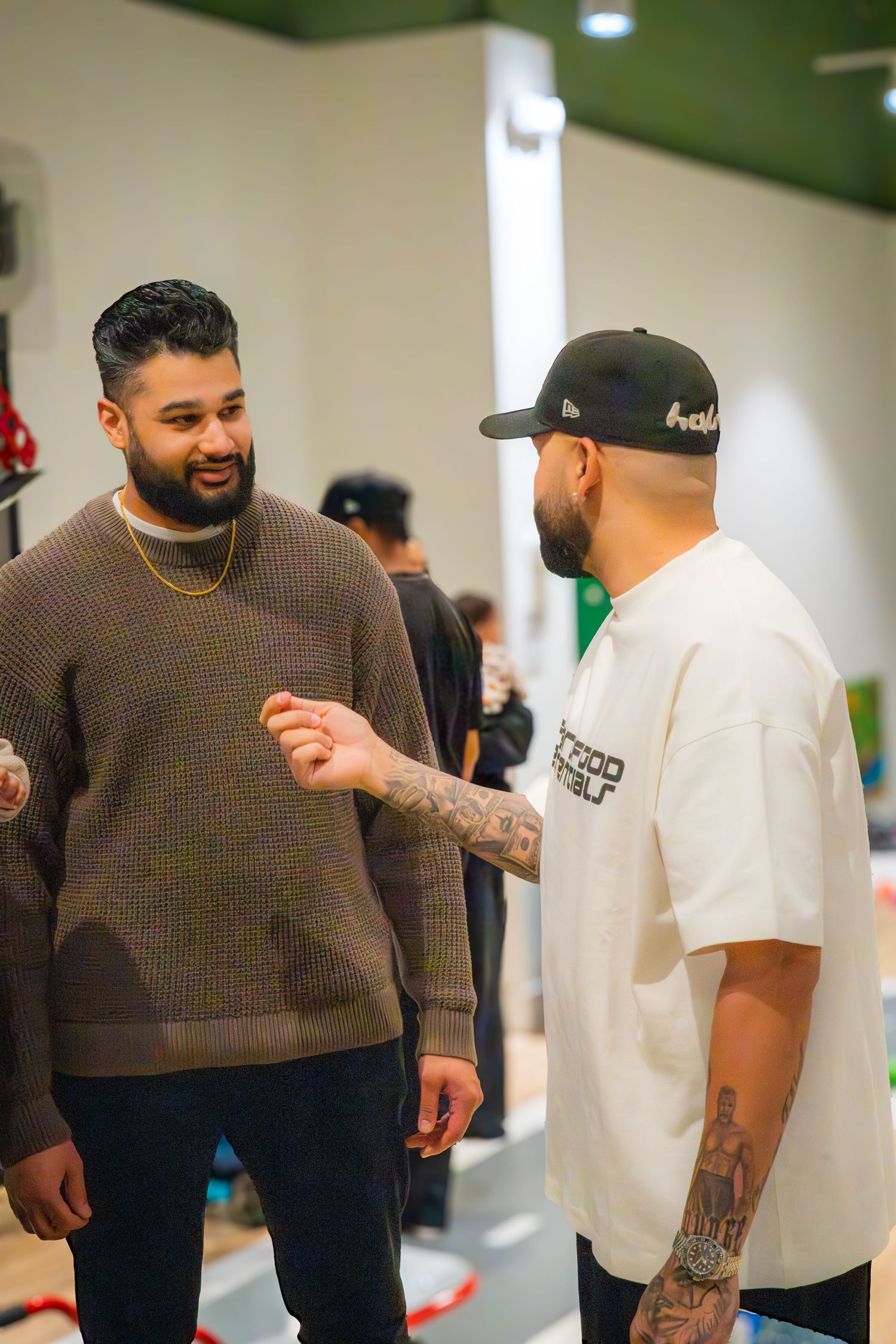 Two tattooed men in casual streetwear having a conversation inside a retail store.