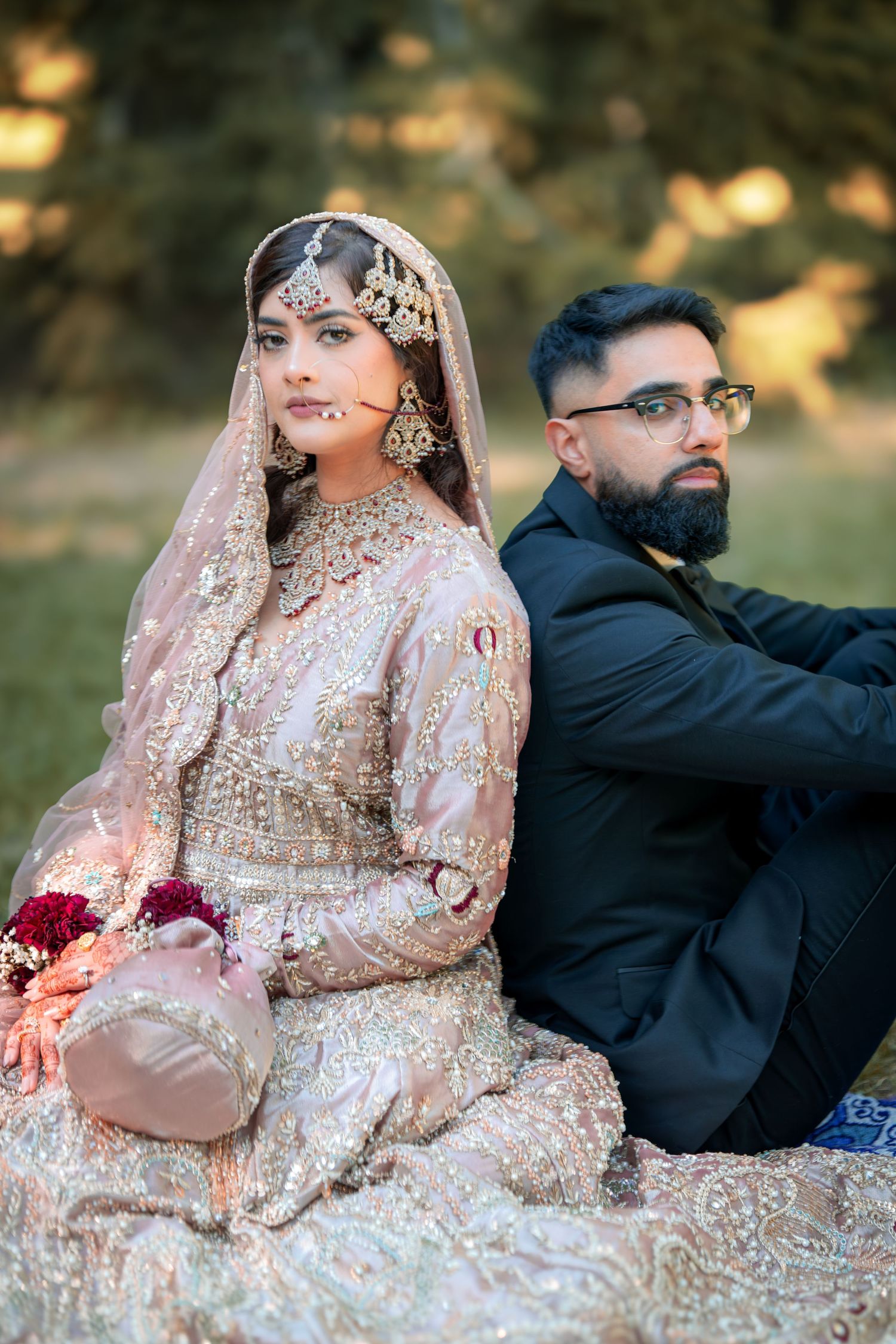 Elegant couple in formal attire pose on grass during sunset photo session.