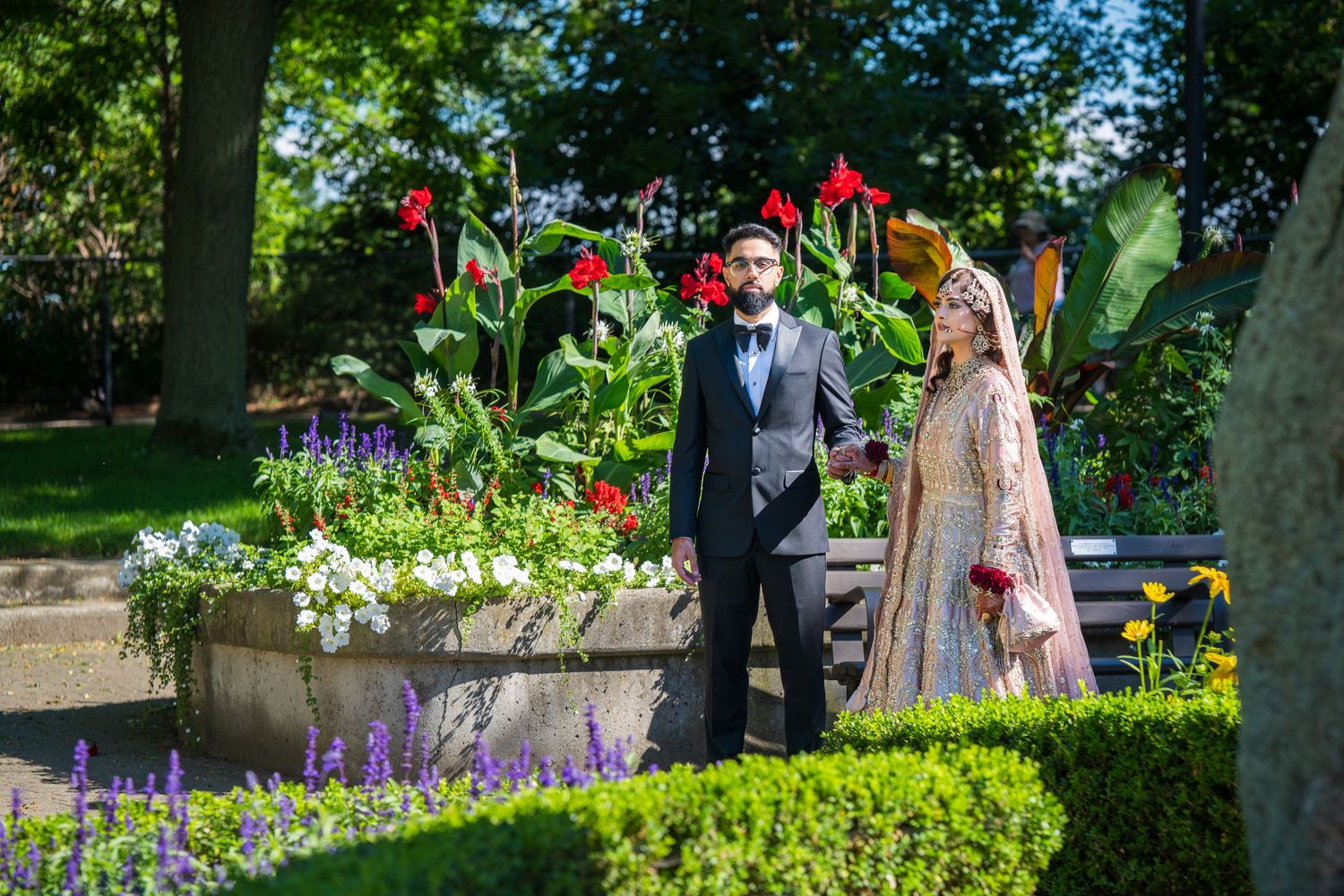 People gather in a lush garden setting with blooming flowers and manicured hedges on a sunny day.