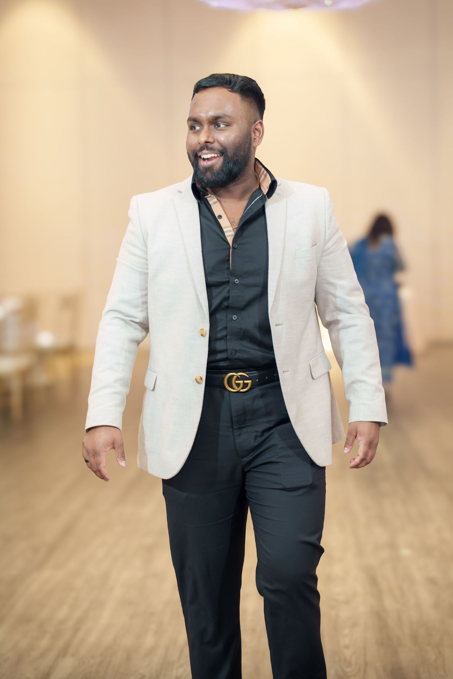 Man in white blazer and black shirt walks confidently across wooden floor.