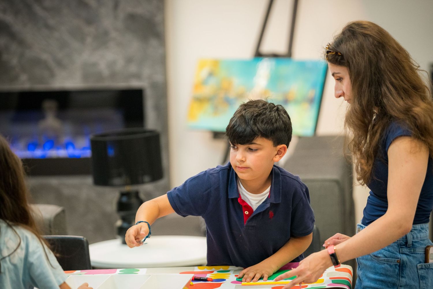 Art instructor guides young student in selecting colorful paper pieces during hands-on children's workshop.