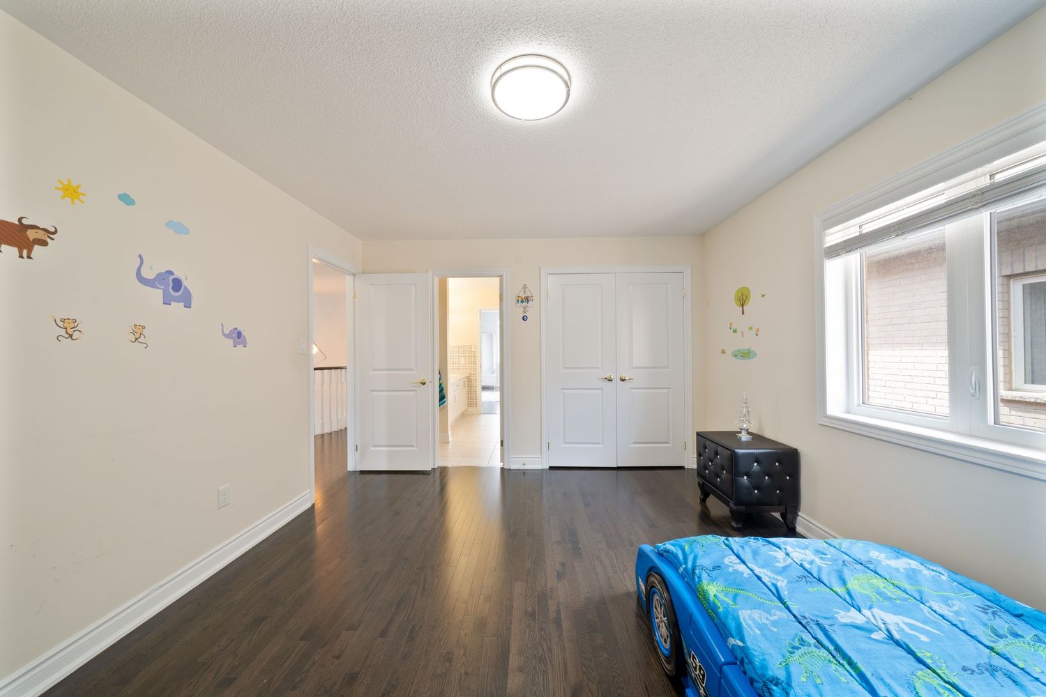 Modern bedroom interior with white walls, hardwood floors, and a blue bed under a window with natural light.