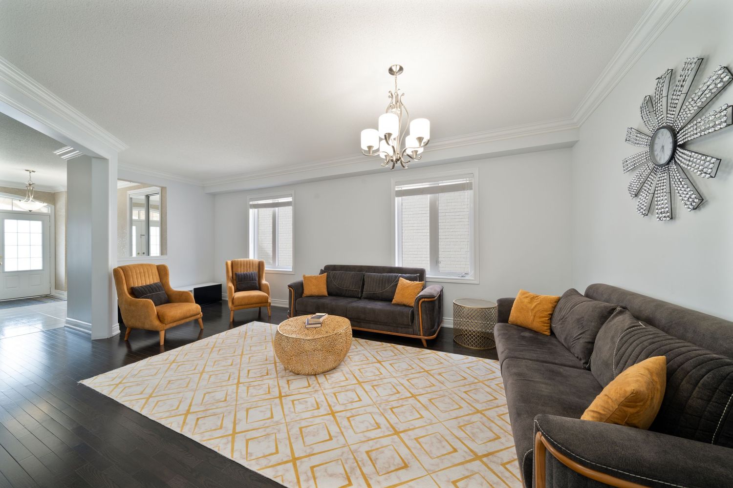 Modern living room interior with gray sectional sofa, orange accent pillows, and geometric pattern area rug.