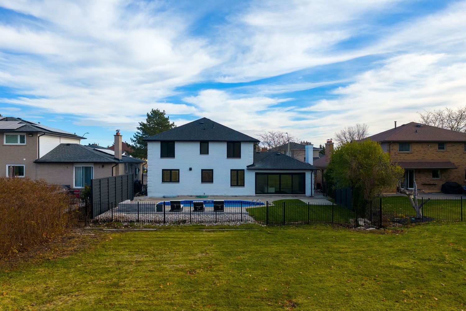 Panoramic view of suburban homes with green lawns against a vibrant blue sky with wispy white clouds.