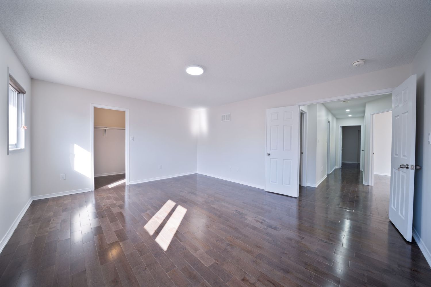 Long modern hallway with polished hardwood flooring, white walls, and recessed lighting creating a bright, minimalist space.