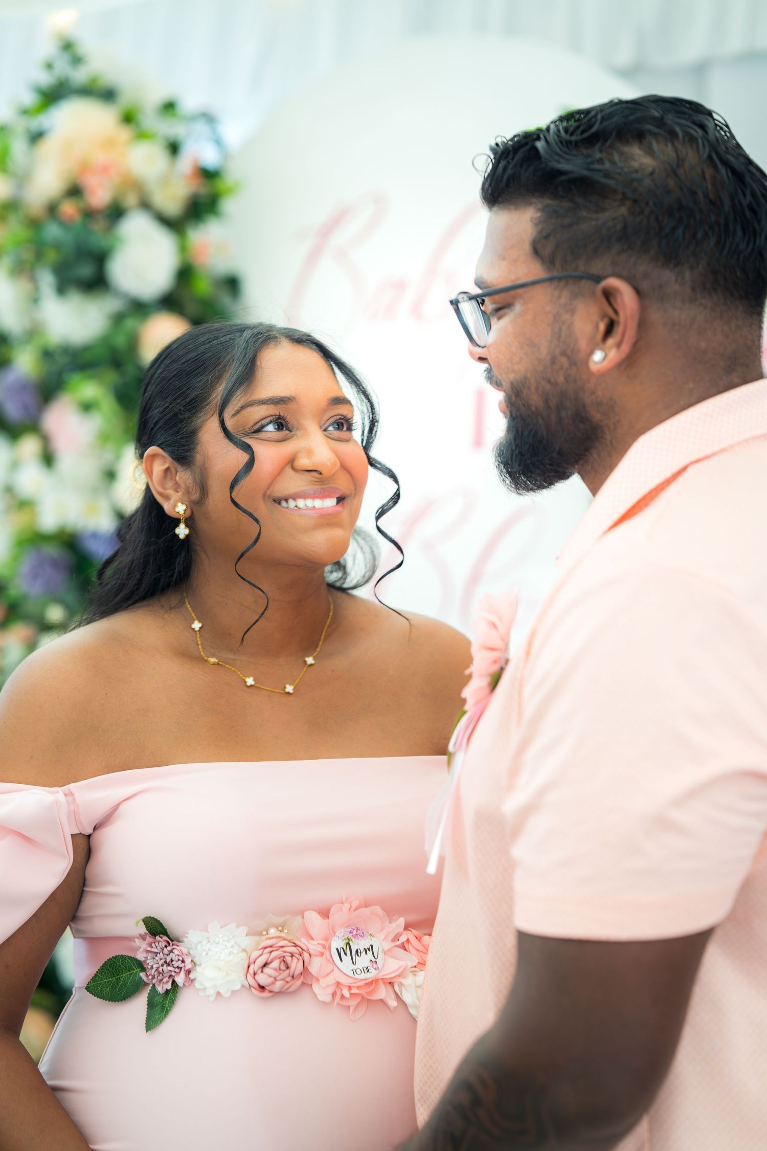 A couple shares romantic moments in front of an elegant floral wall display.