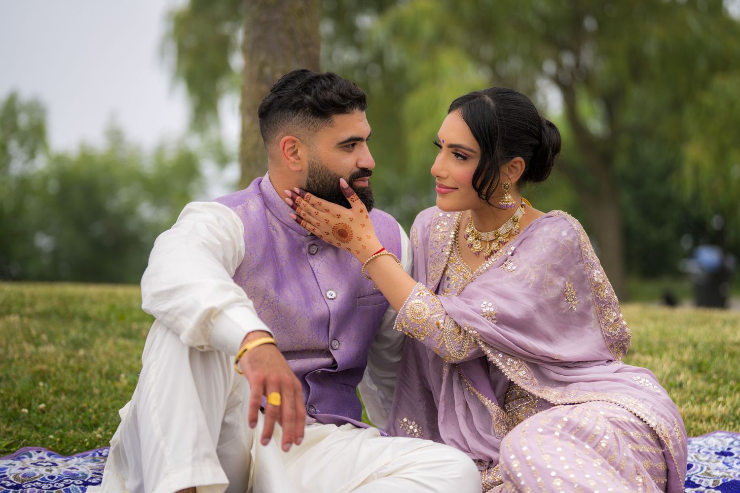 Romantic outdoor photoshoot featuring couple in traditional South Asian attire relaxing on blue blanket.