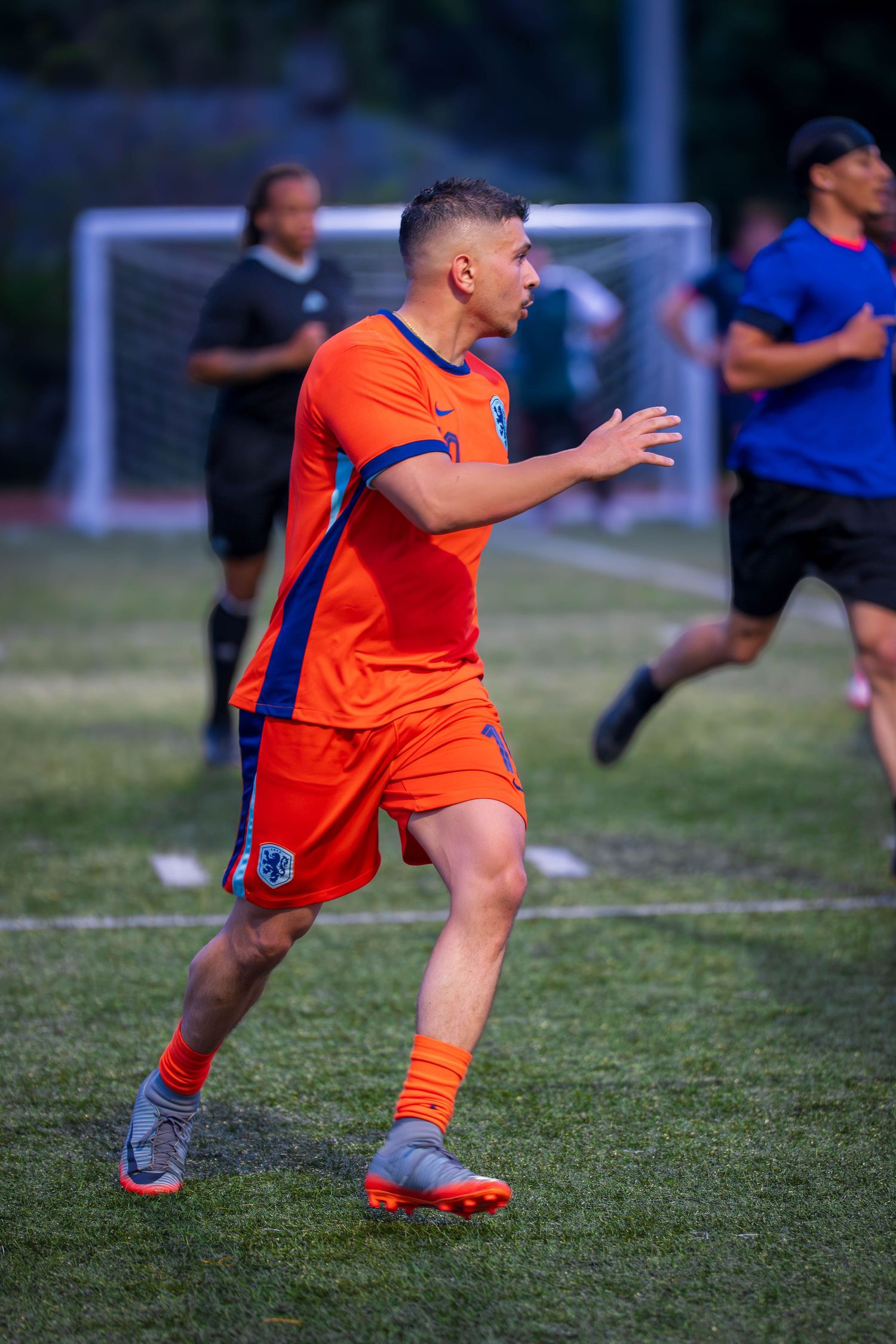 Athlete in orange jersey runs across soccer field during competitive match.