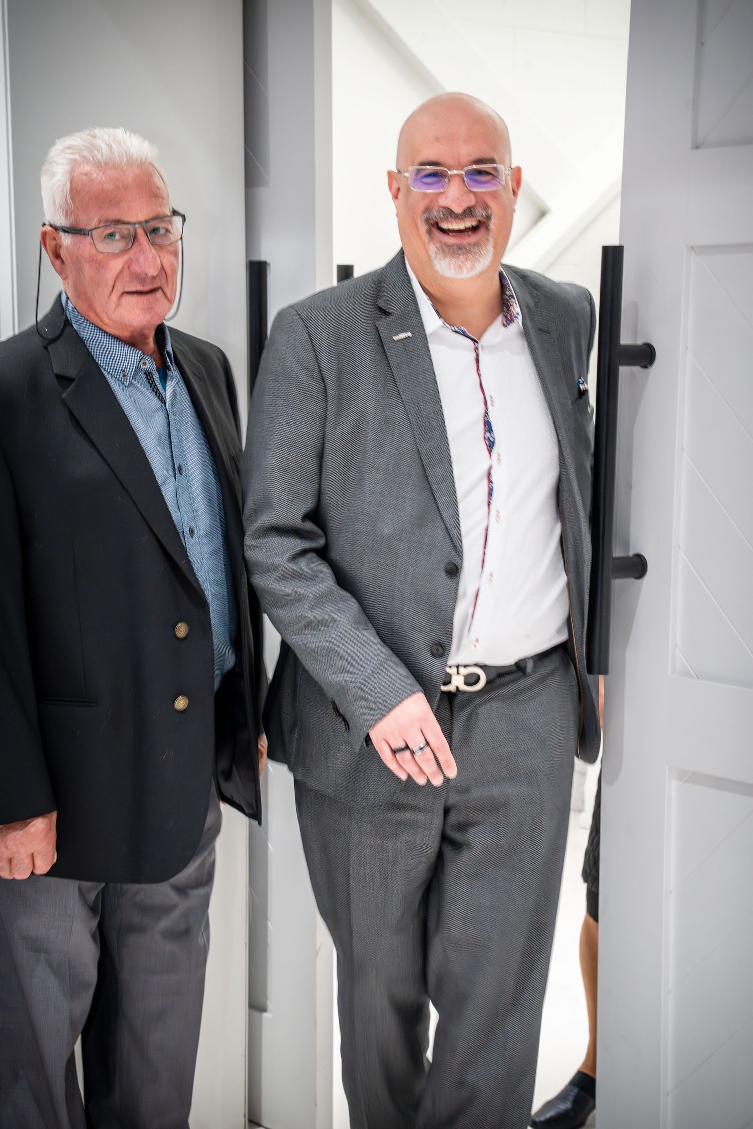 Business professionals engaged in conversation by a white door in an office hallway.