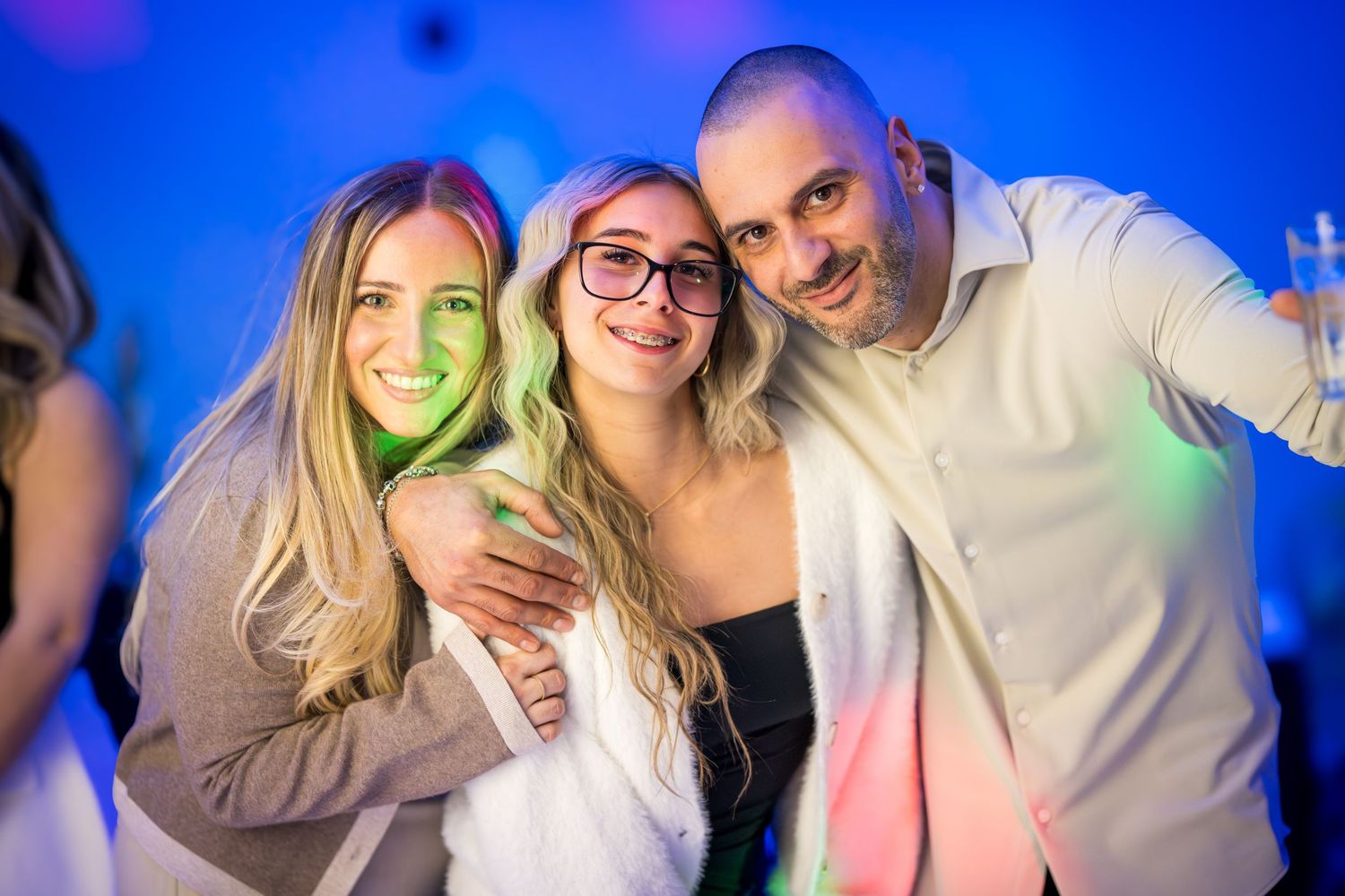 Group celebrating and posing together under vibrant blue party lights.