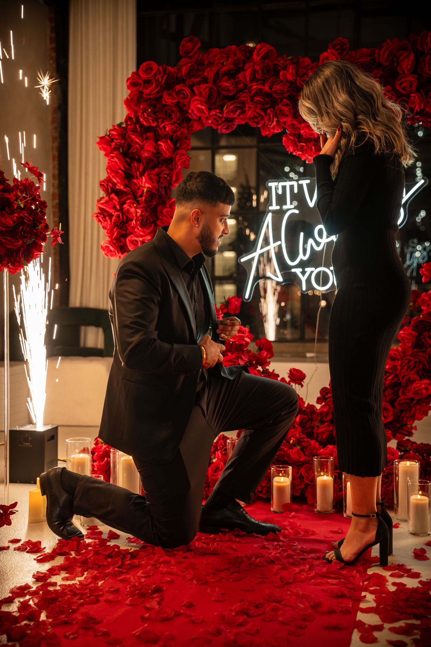 Marriage proposal moment captured against a backdrop of red roses and neon lighting.