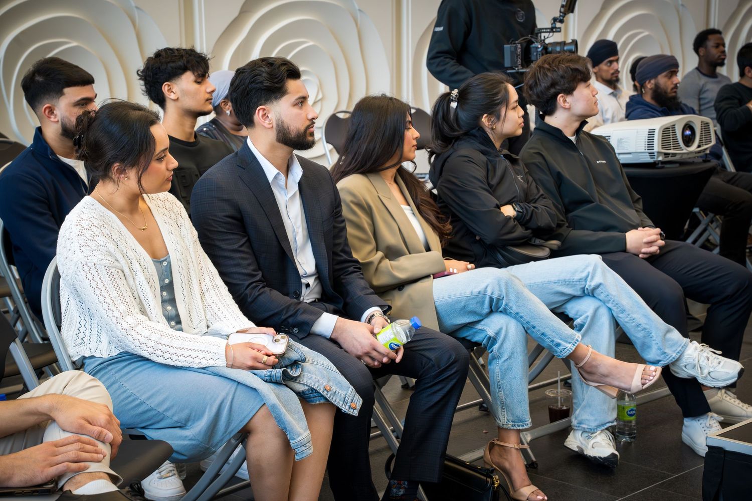 Professional audience members in business casual attire watching presentation in modern venue.