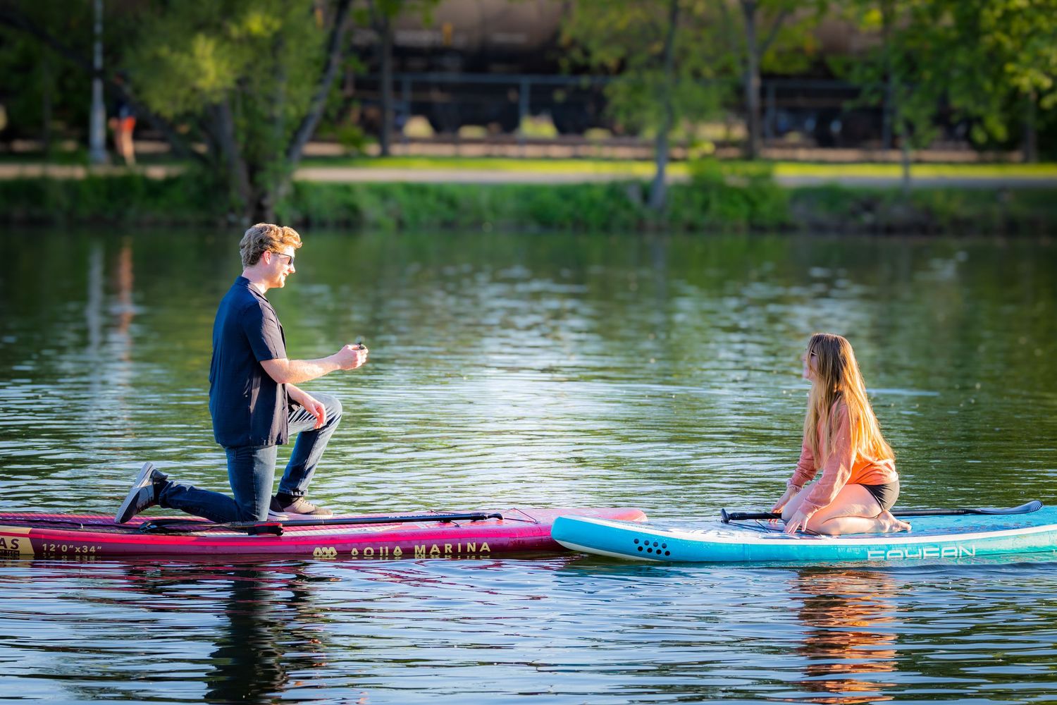 Man proposing on a paddleboard to a woman on a calm lake on a sunny day.