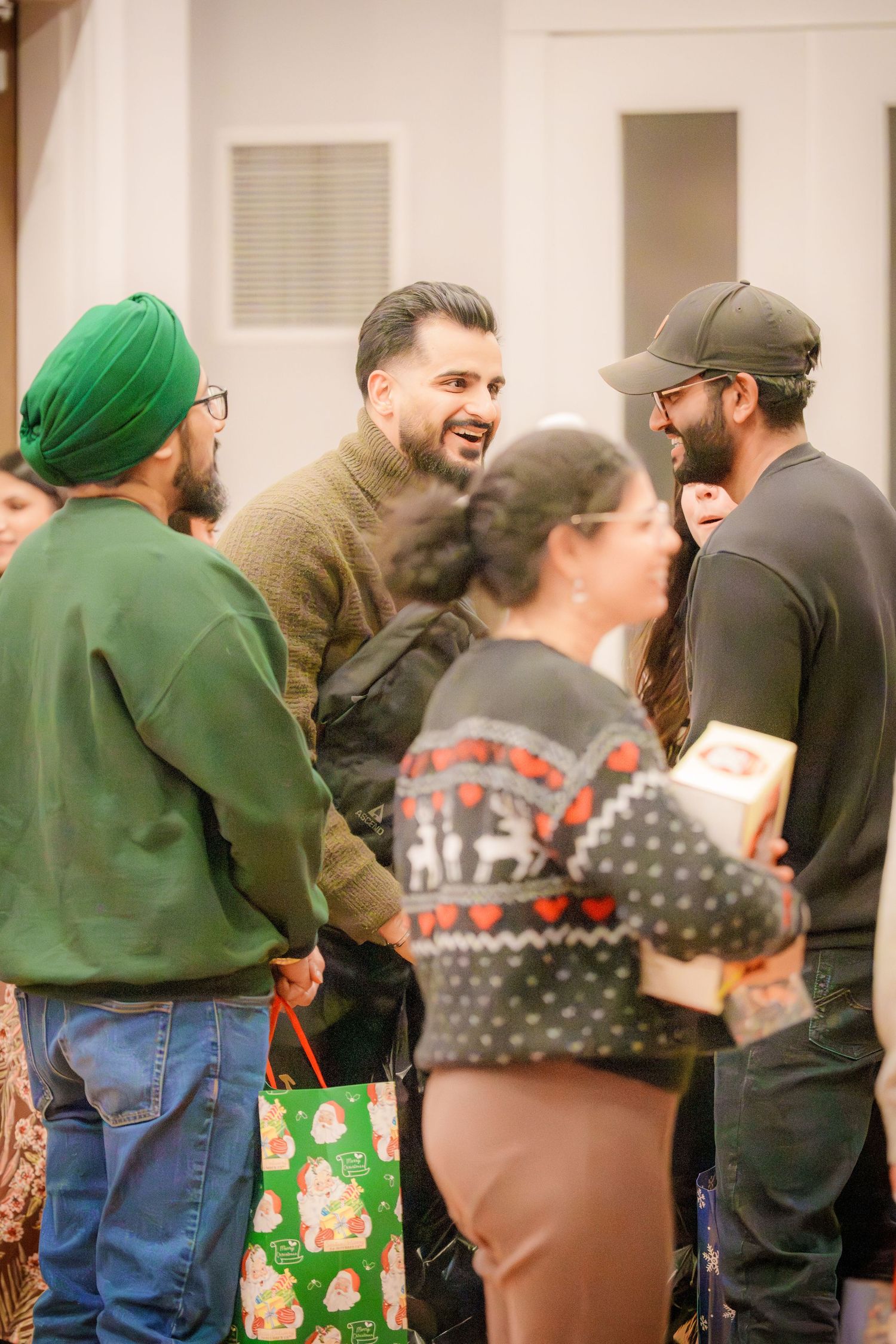 Group of people chatting and socializing at a casual indoor holiday gathering with gift bags visible.
