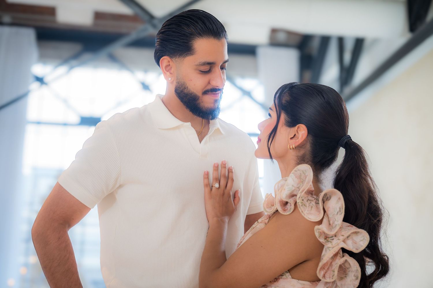 Close-up of couple gazing at each other, woman showing off engagement ring in soft light.
