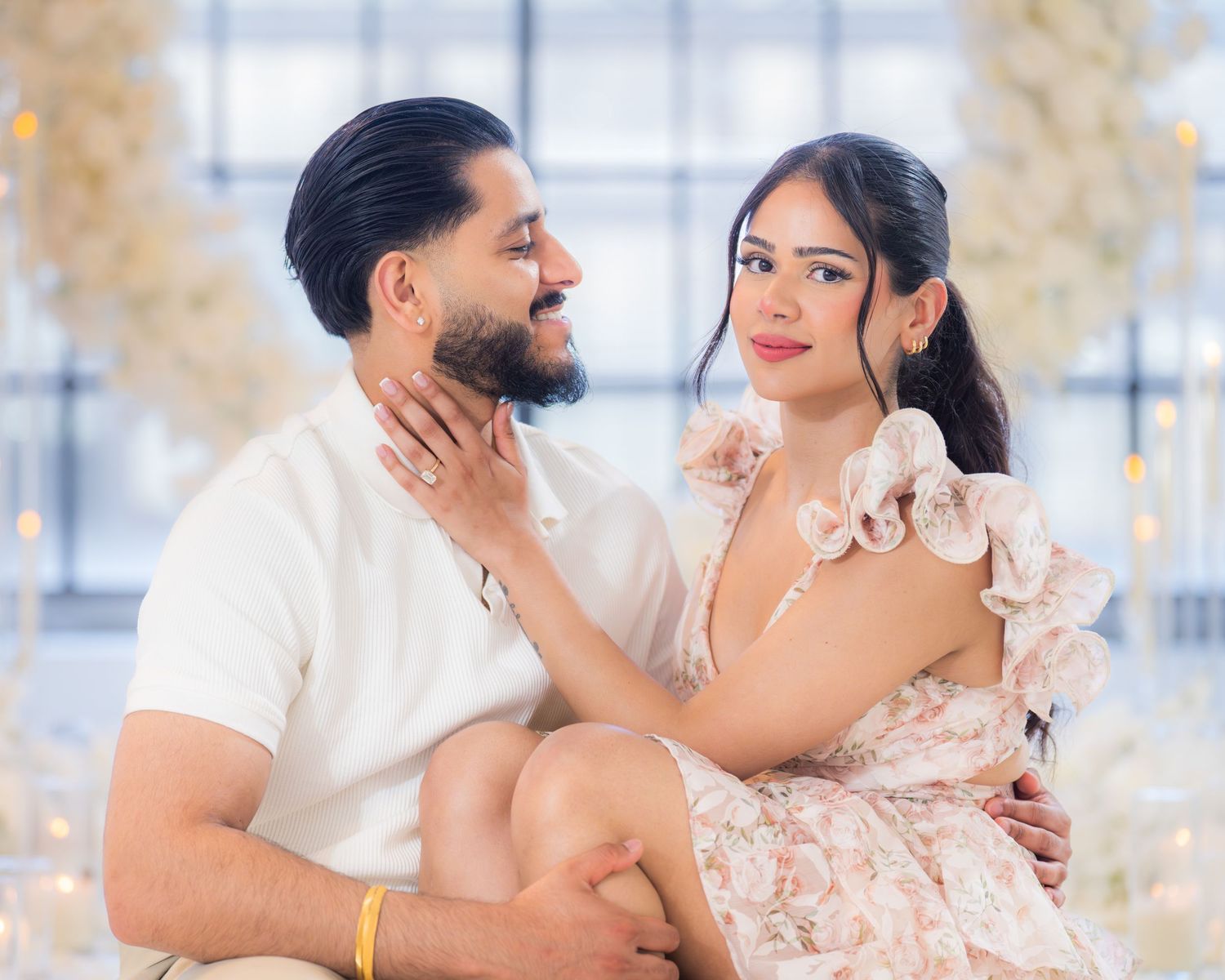 Couple sitting closely together, gazing lovingly at each other with white florals behind.