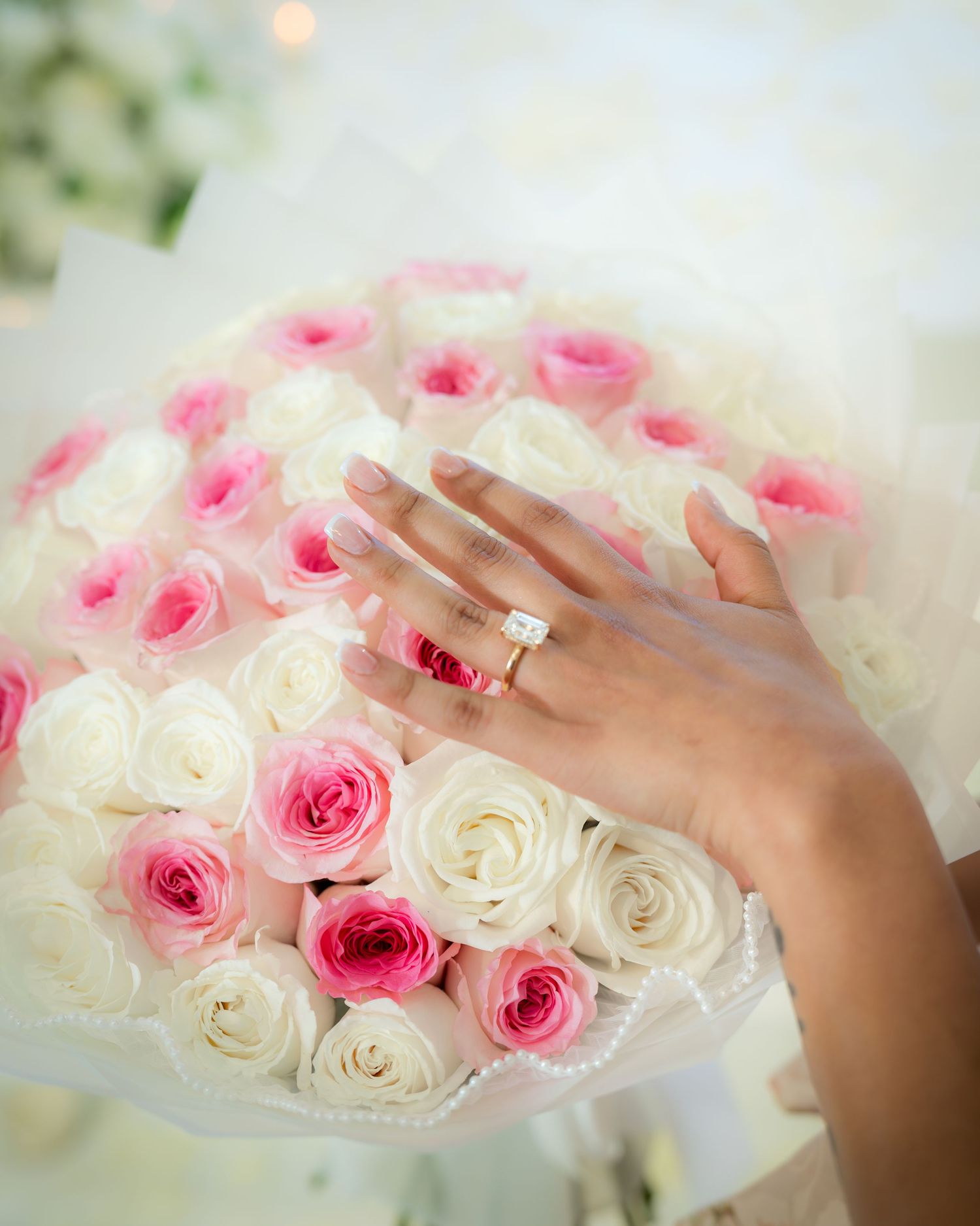 A newly engaged woman displays her diamond ring over a bouquet of pink and white roses.