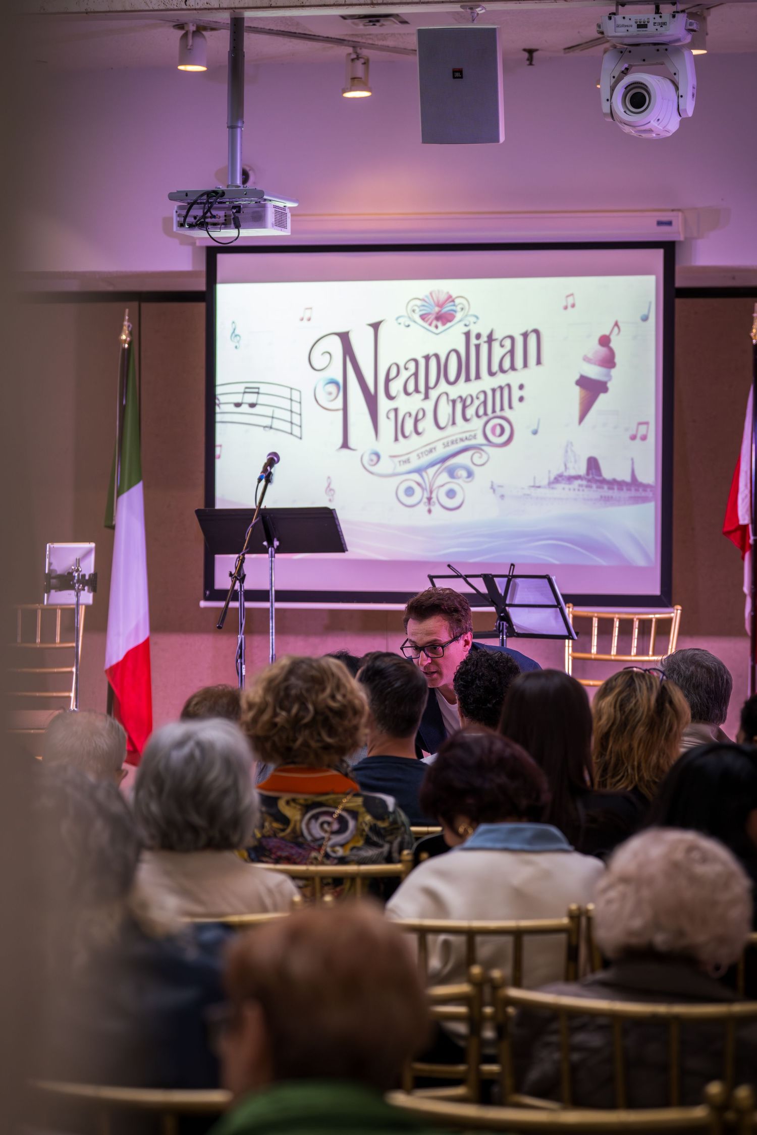 Audience watches a Neapolitan Ice Cream themed presentation on a large screen at an indoor event.