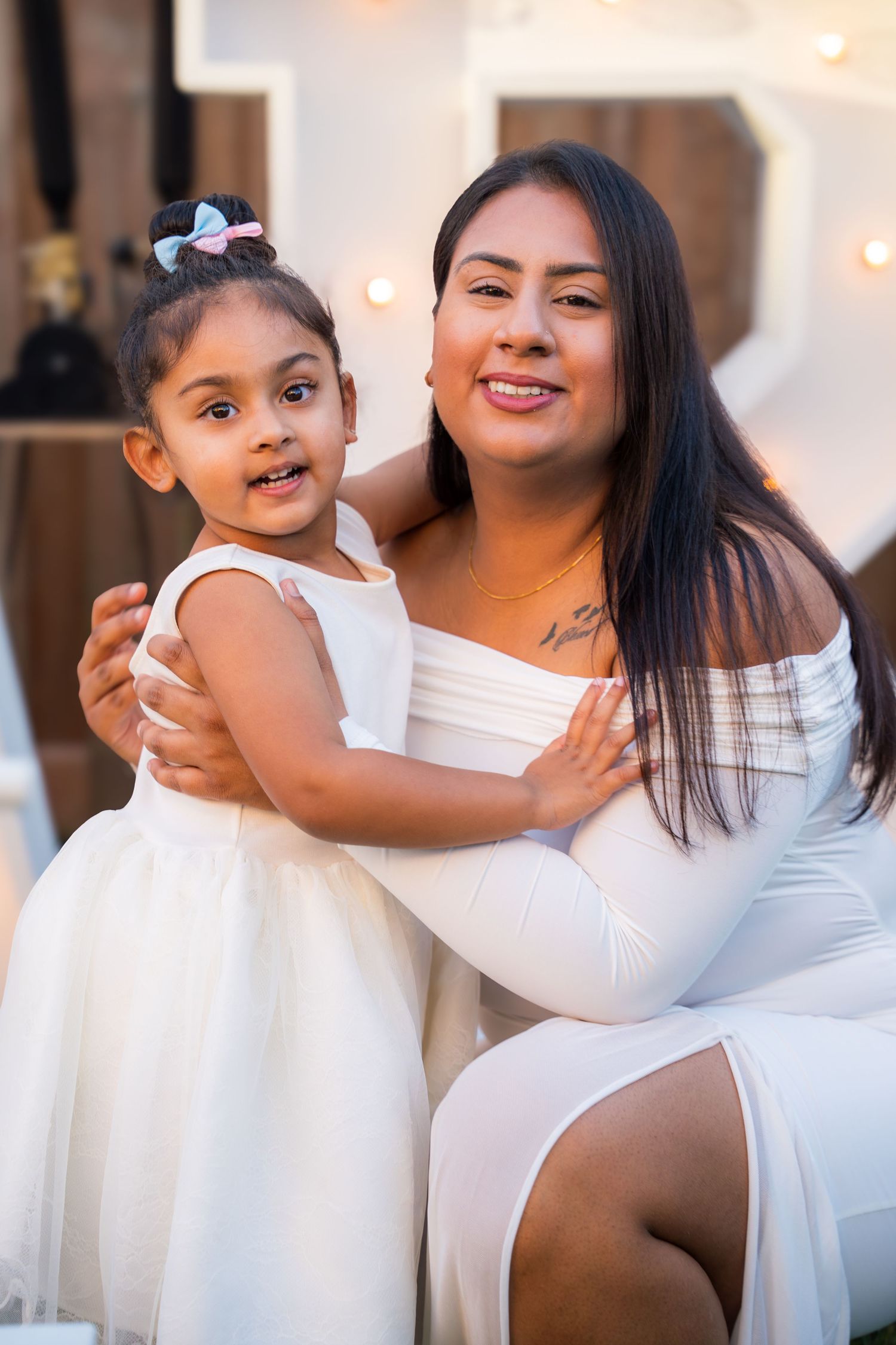 A woman in a white dress holds a little girl in a white tutu at a gender reveal party.