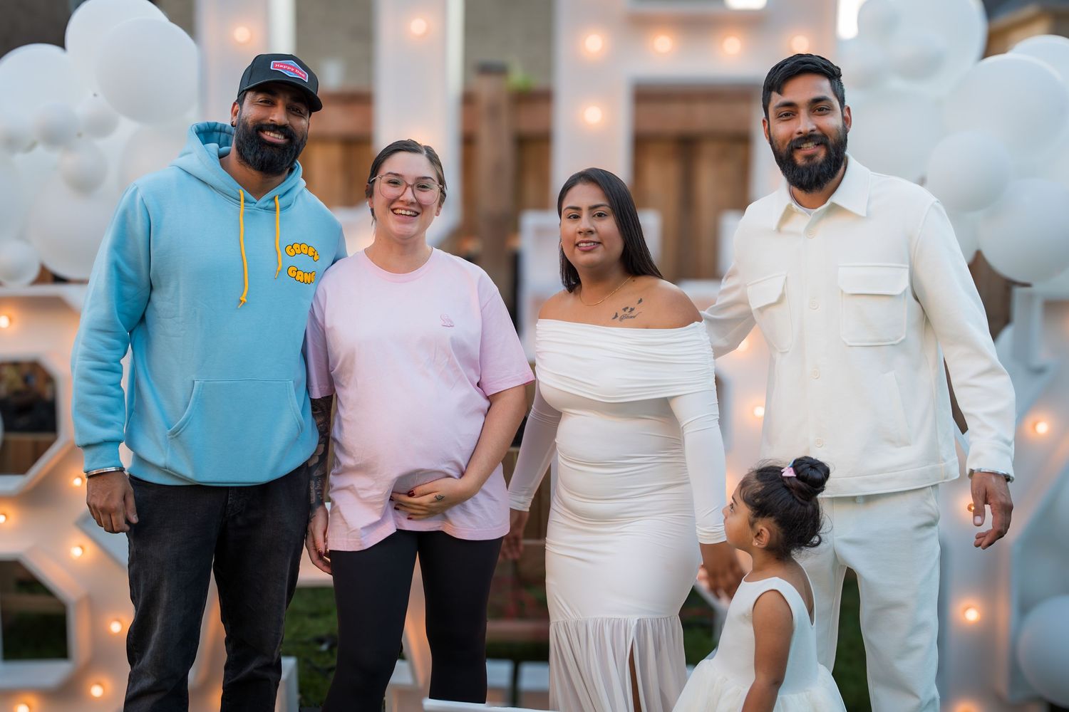 Group of five smiling adults and child pose outdoors at a gender reveal celebration at night.