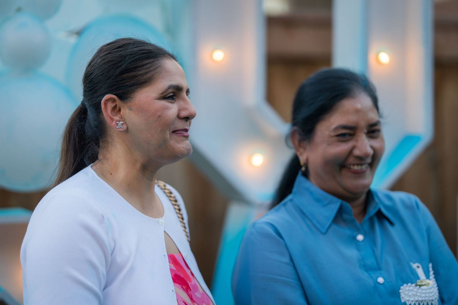 Two older women smiling together at an outdoor gender reveal party with blue decor.