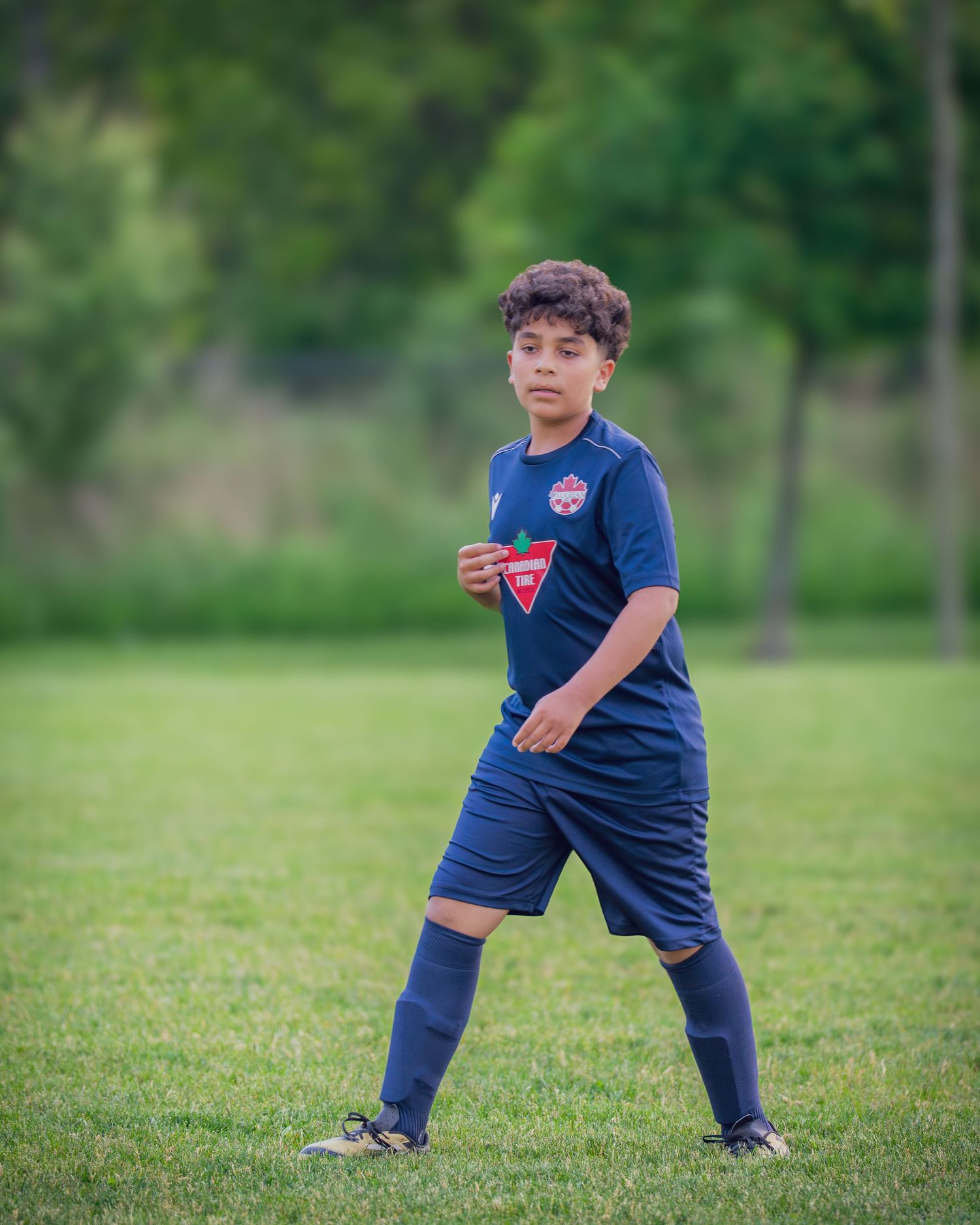 A young child in a navy blue shirt and pants practices martial arts stances on a grassy field.