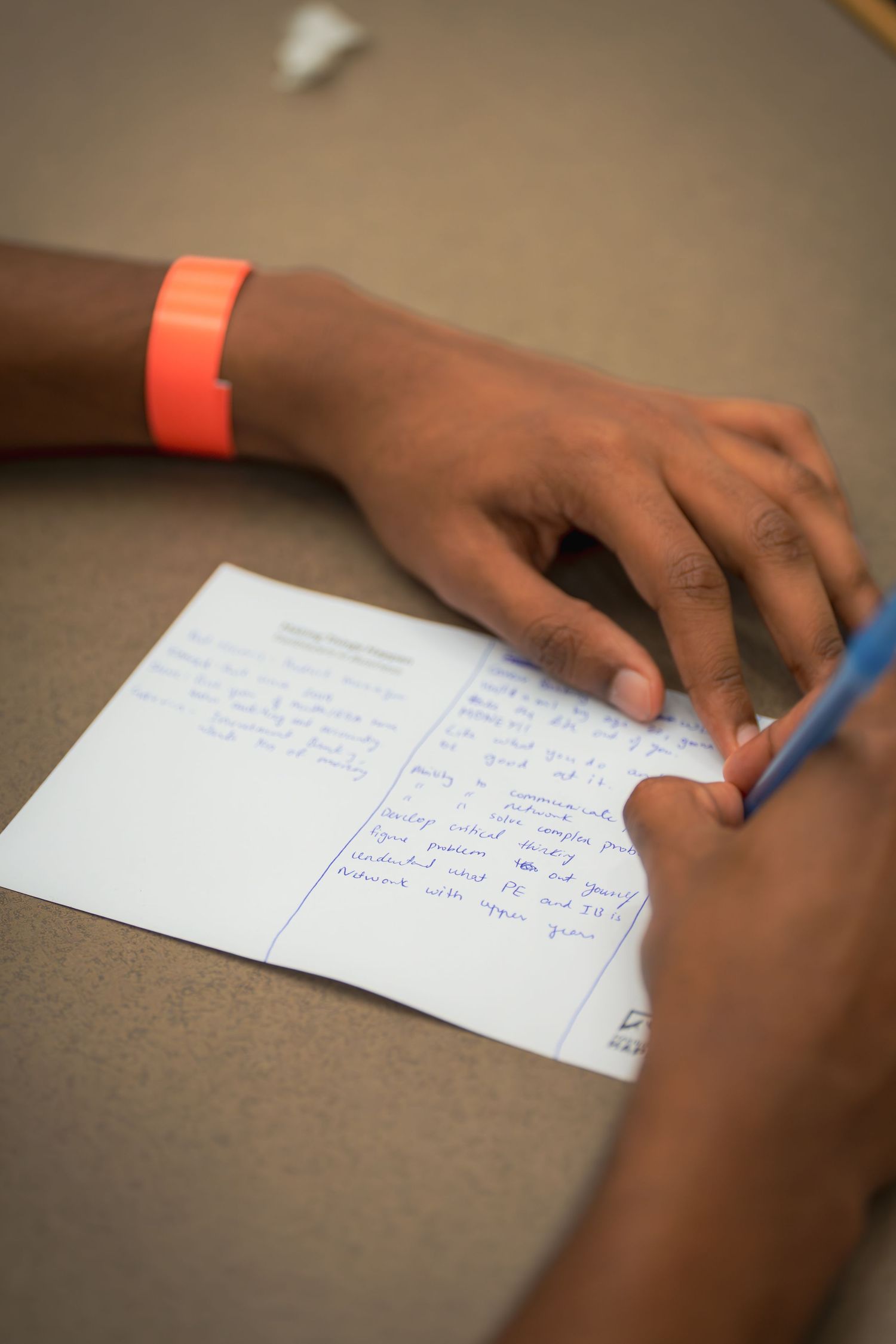 Close-up of hands writing notes on white paper with blue pen during a study session.