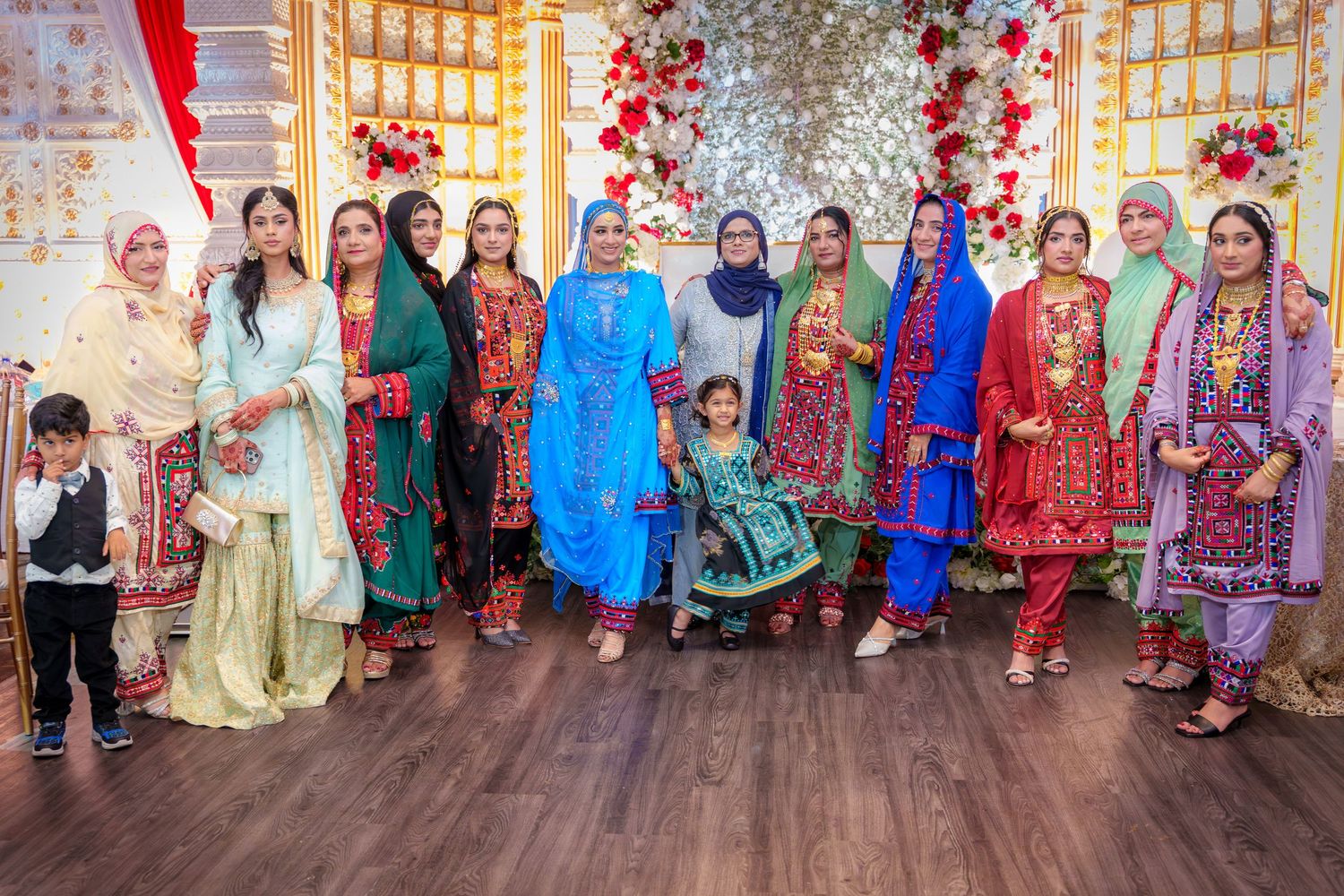 Group photo of wedding guests in colorful traditional South Asian attire against floral backdrop.