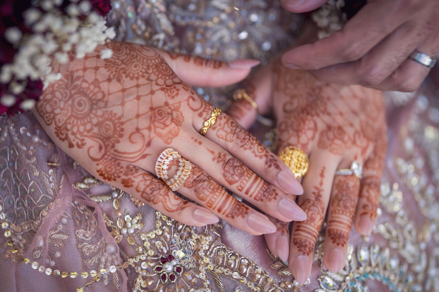 Traditional henna designs adorn hands against an ornate embroidered fabric background.