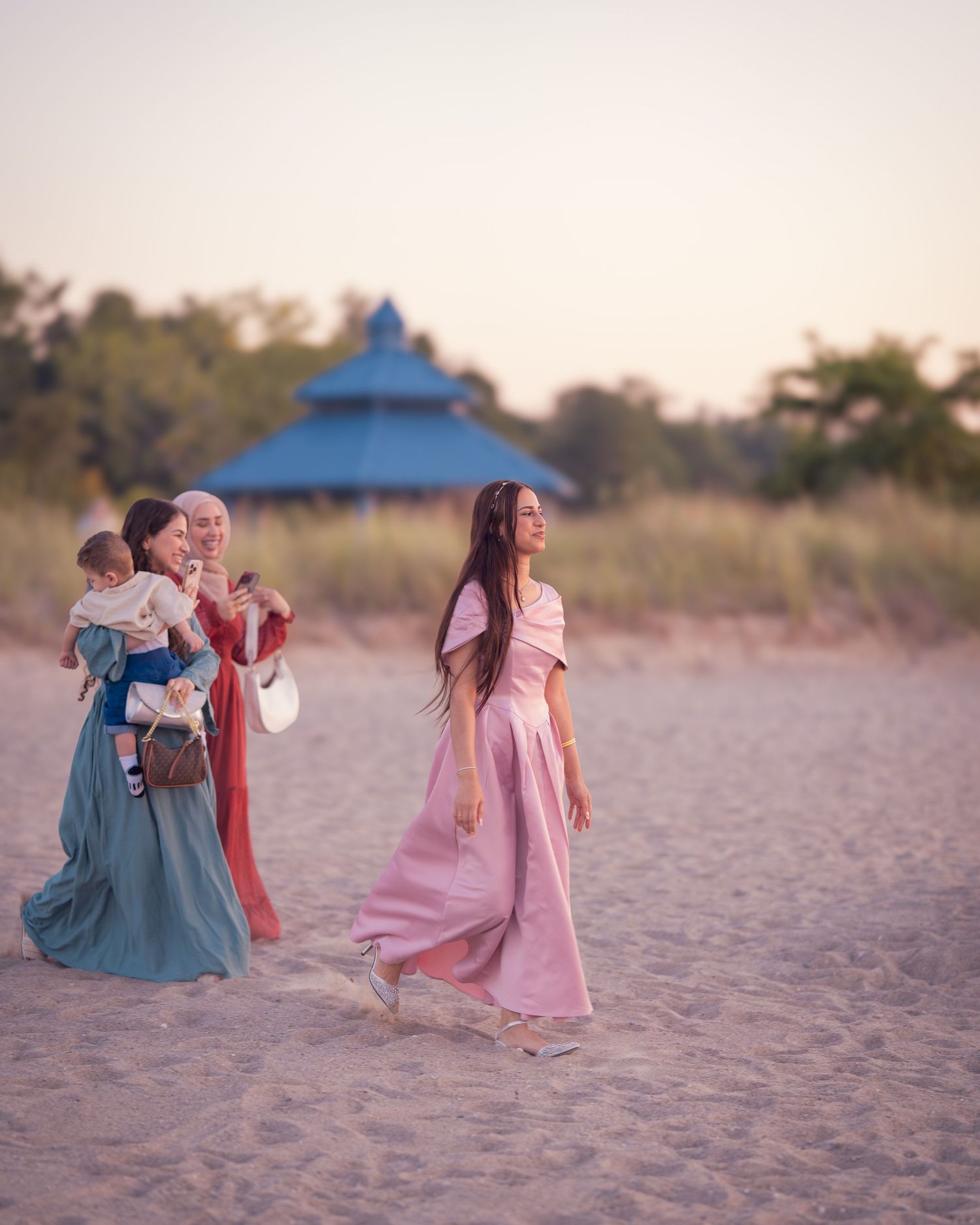 People walking together on a sandy beach at sunset wearing pink and blue outfits.