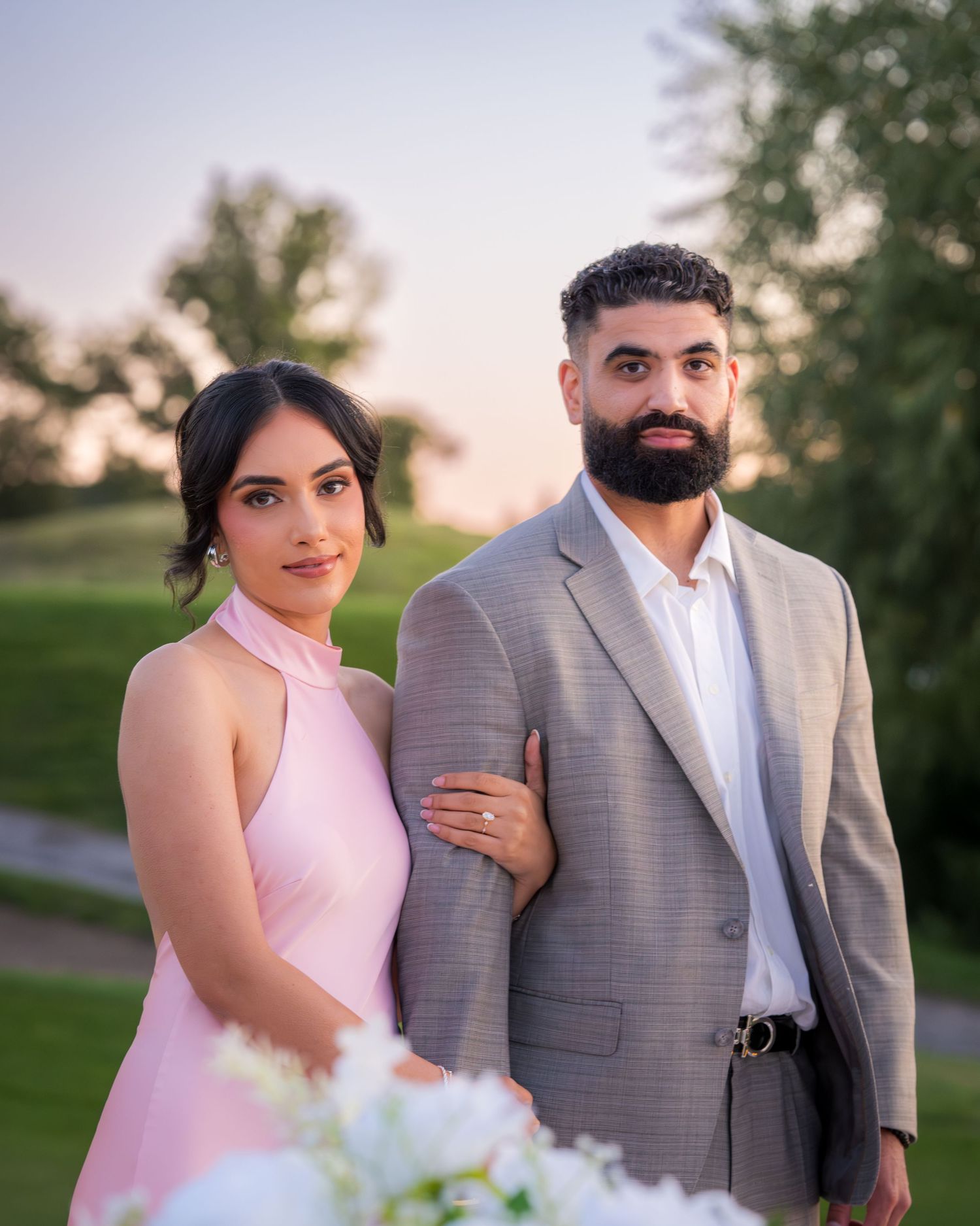 Couple poses together during golden hour with white floral decorations.